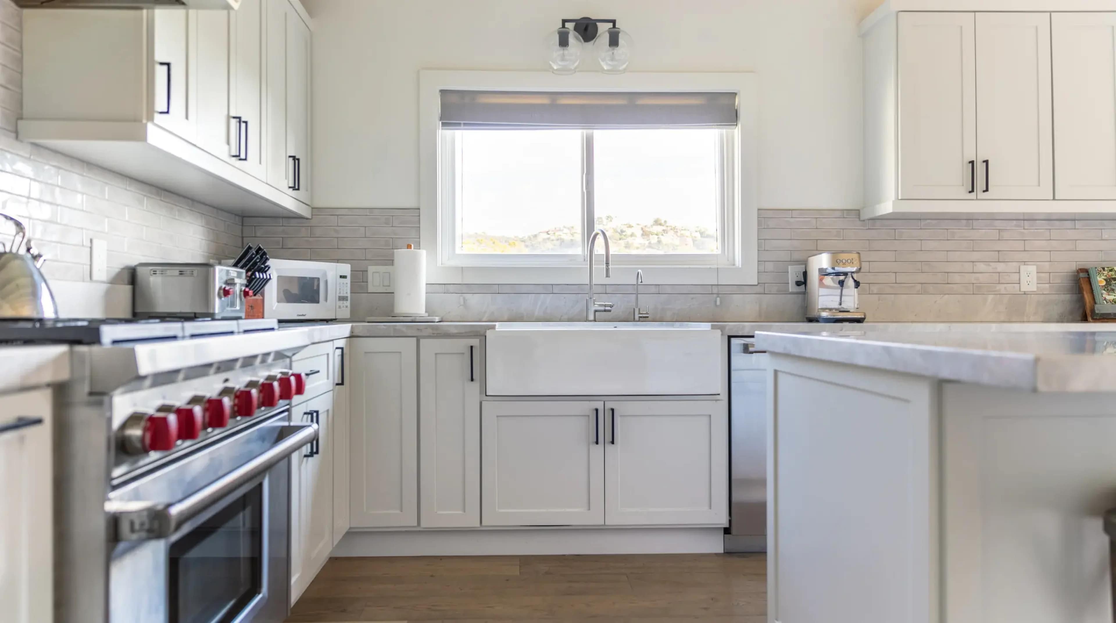 A modern kitchen with white cabinetry, a farmhouse sink, and stainless steel appliances, centered around a window that overlooks a scenic view.