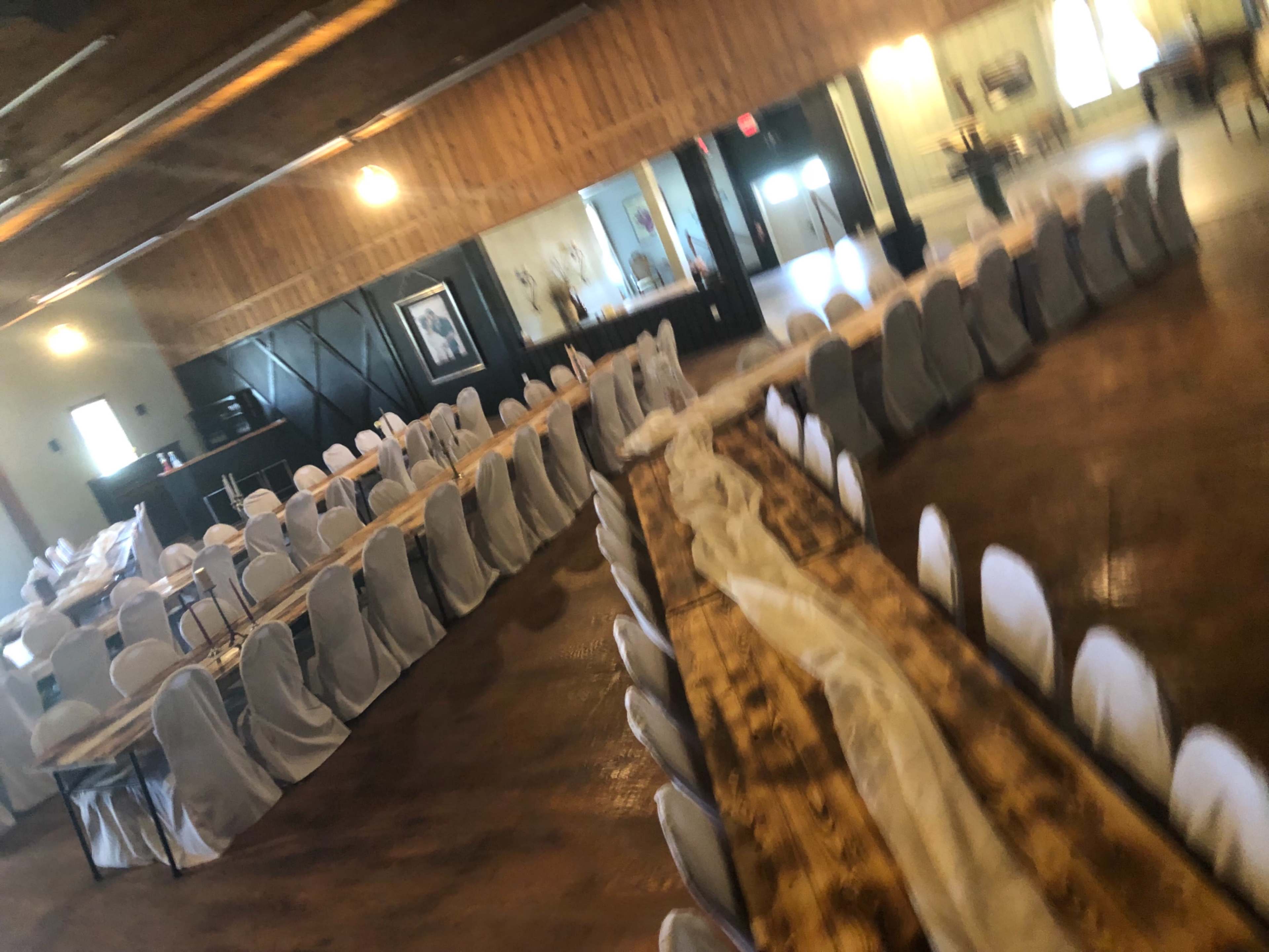 A large banquet hall arranged with long tables covered in white tablecloths and surrounded by covered chairs, ready for an event.