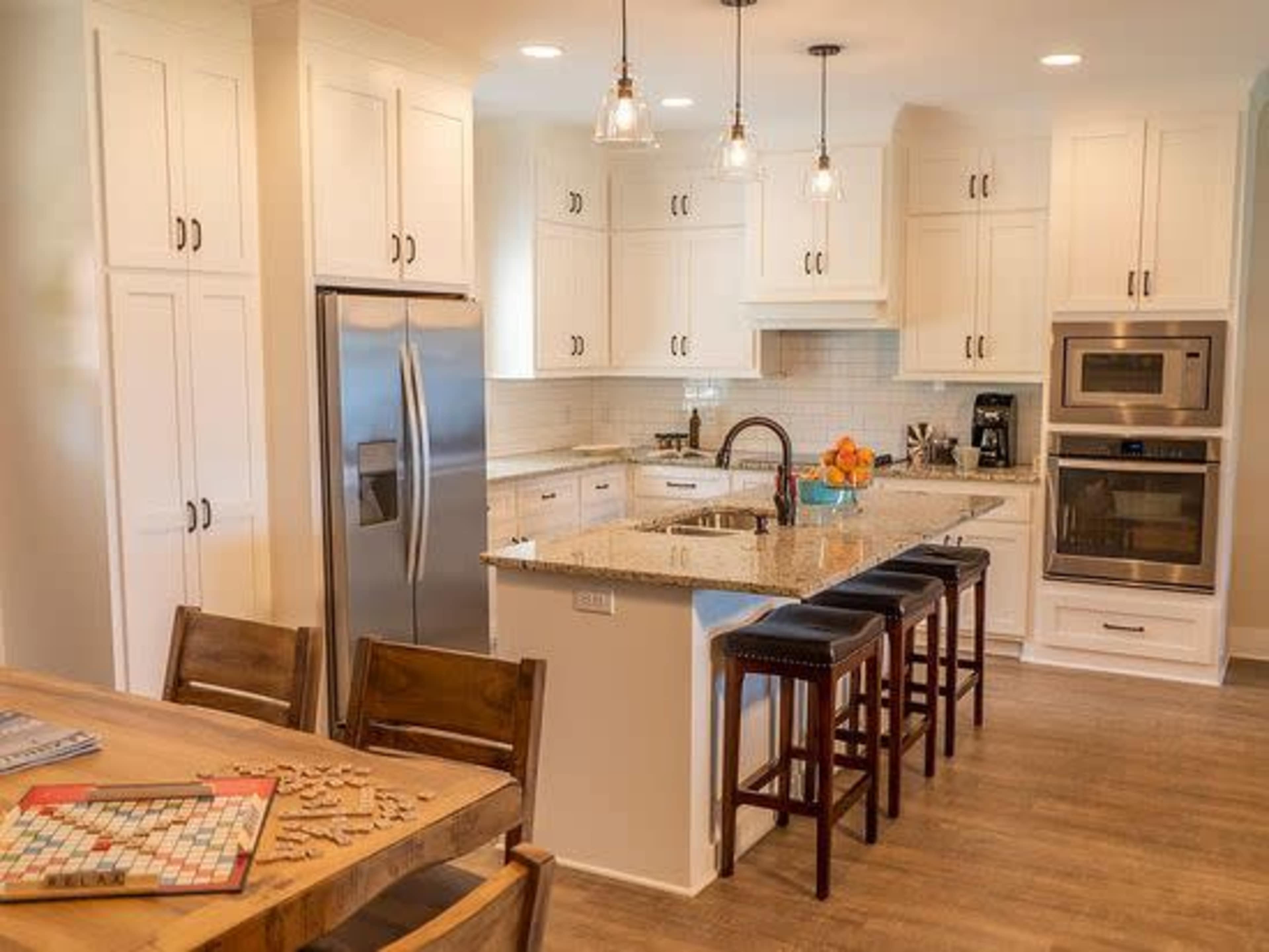 A modern kitchen features white cabinets, a granite countertop island with bar stools, and stainless steel appliances.
