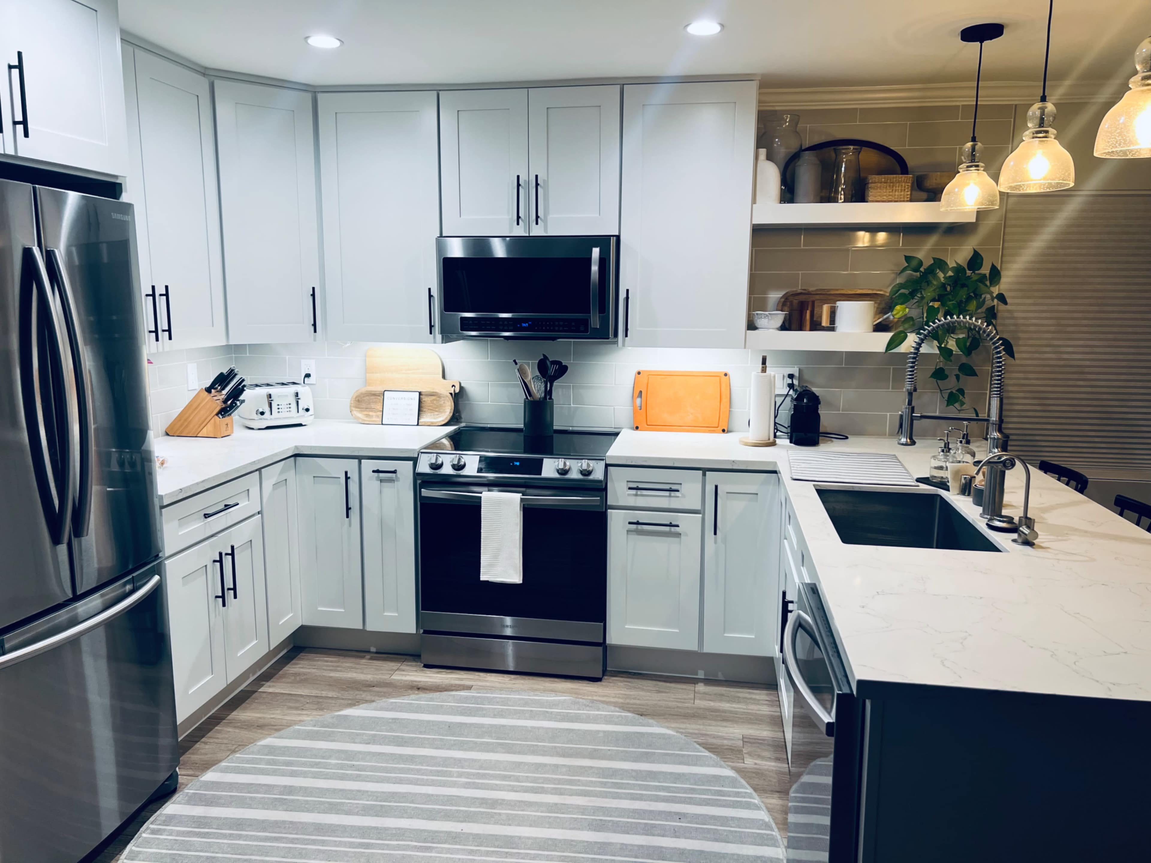 A modern kitchen features light gray cabinets, stainless steel appliances, a marble countertop, and a large circular area rug on the floor.