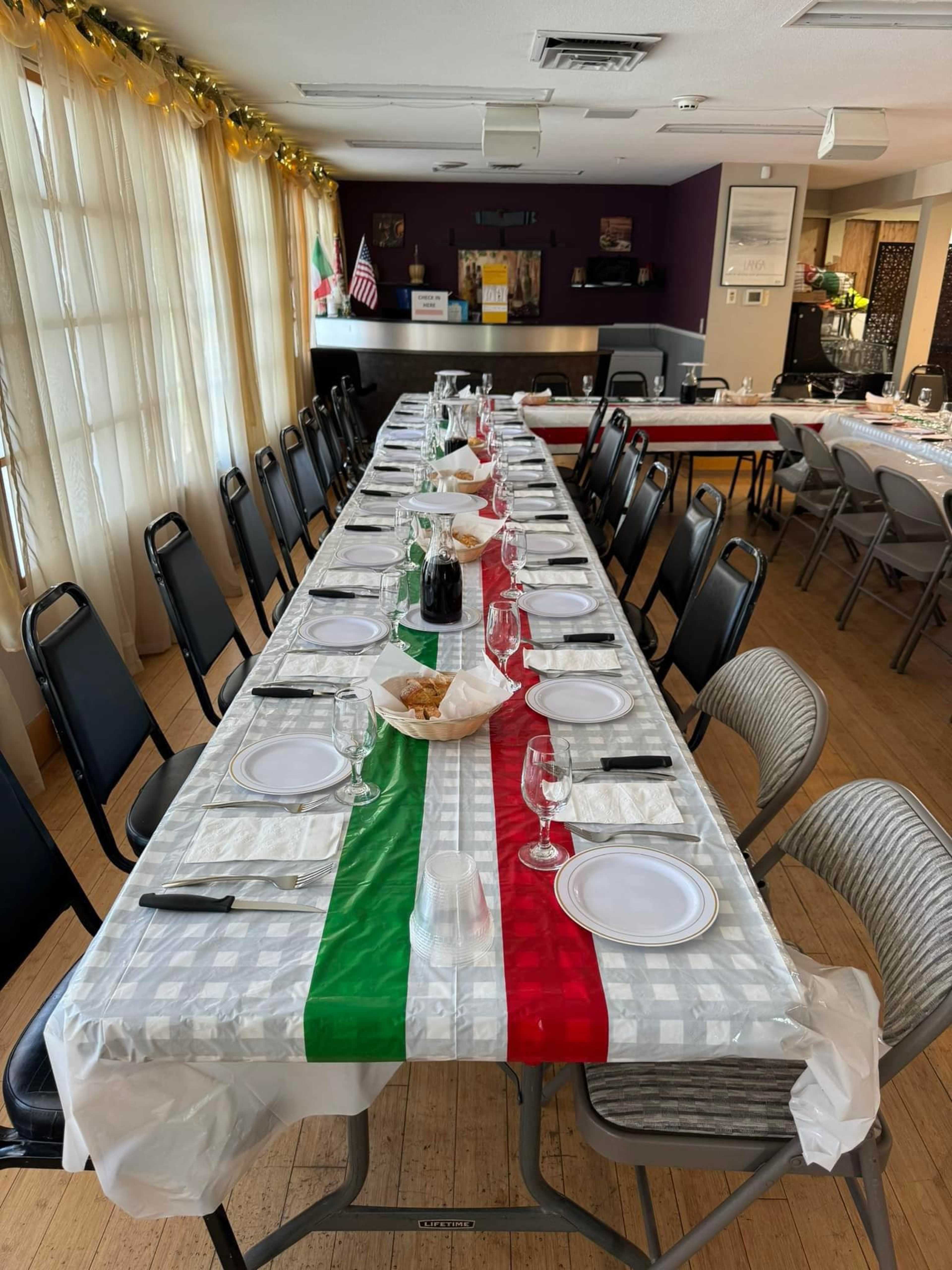A long dining table is set with white plates, glasses, and utensils, adorned with a green, white, and red tablecloth in a decorated dining space.
