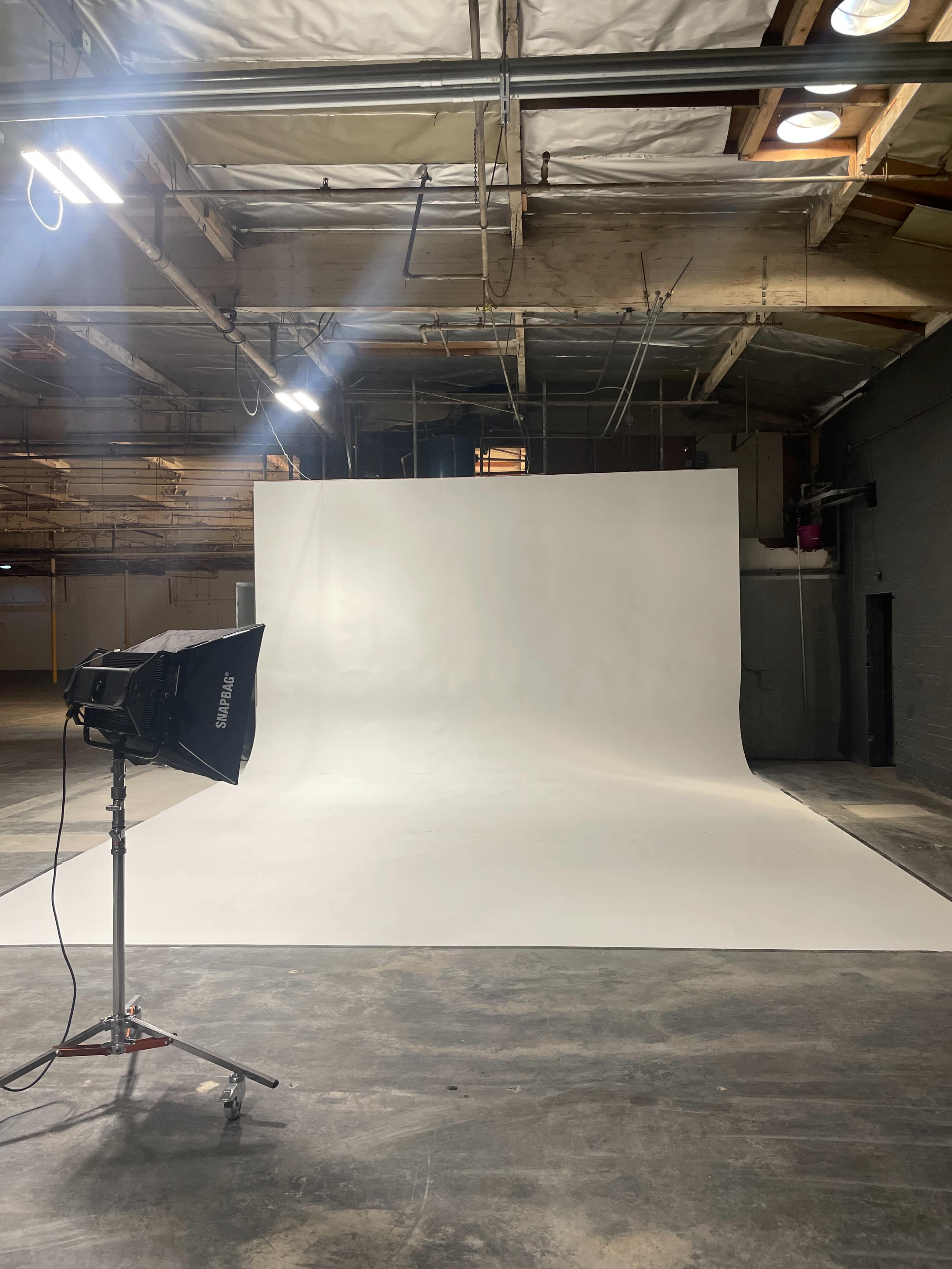 An empty photography studio with a seamless white backdrop and a lighting setup on the left side.
