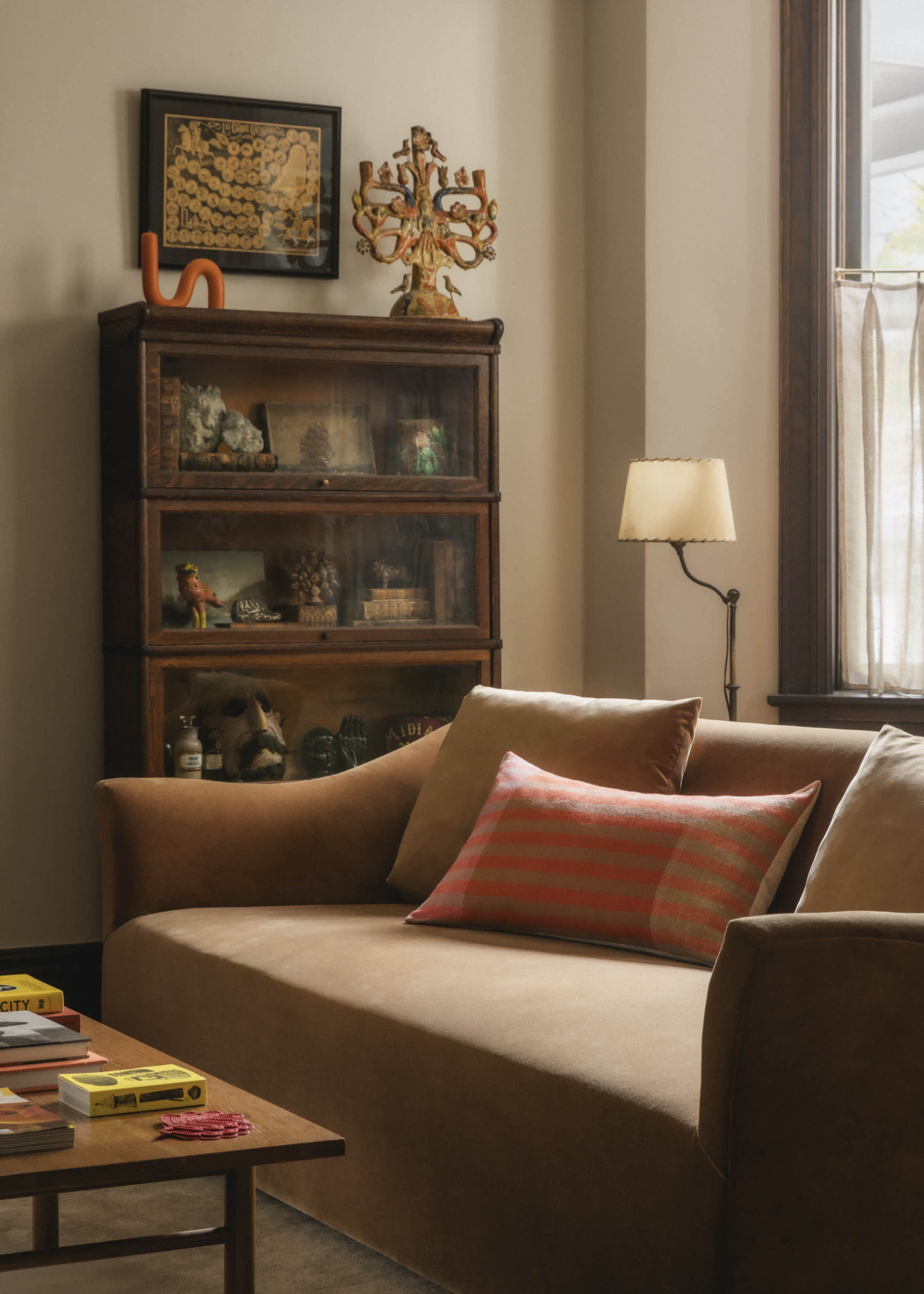 The image shows a cozy living room with a brown sofa, a wooden bookshelf filled with decorative items, and a lamp beside the window.