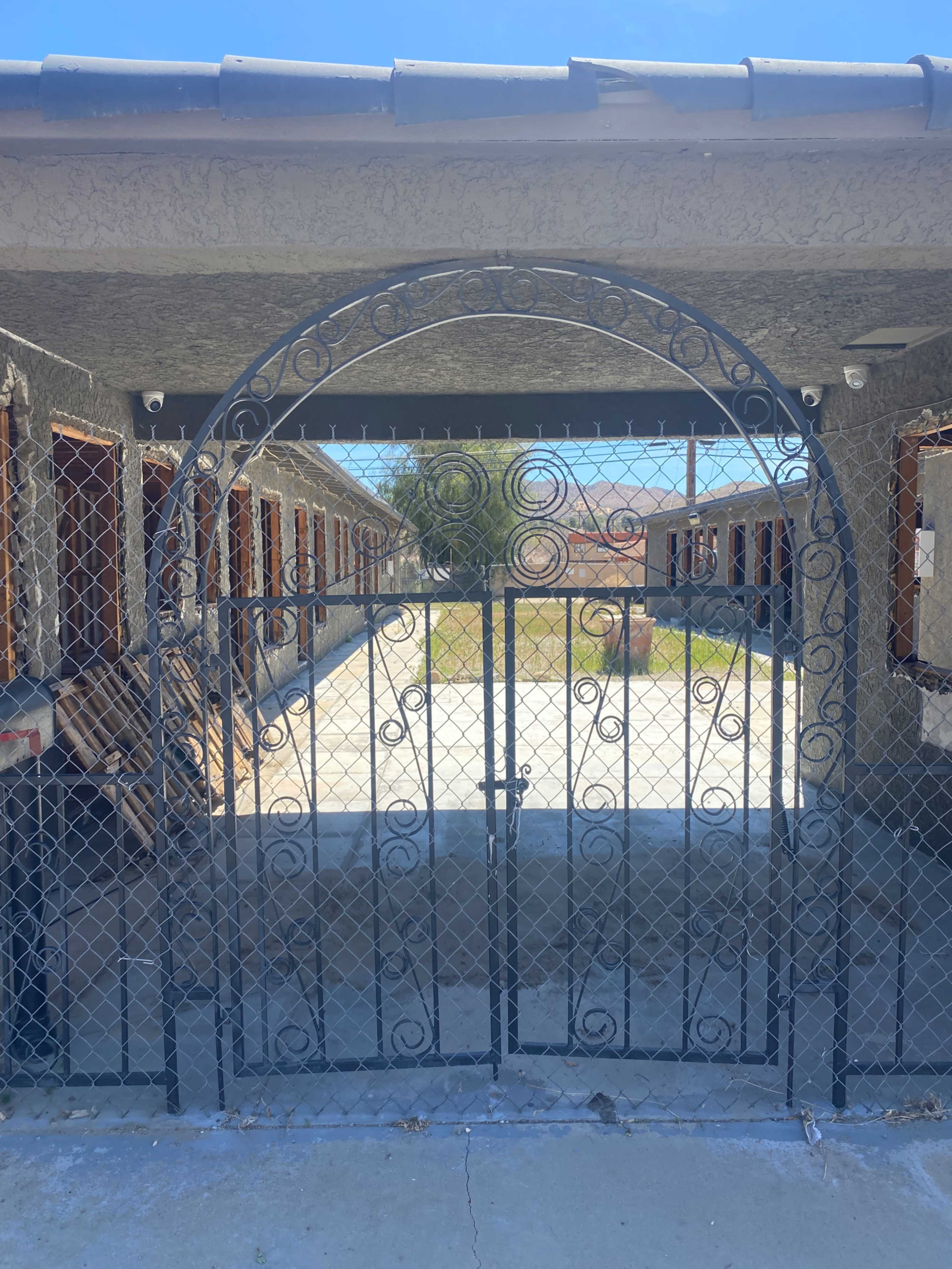 A wrought iron gate, adorned with decorative scrolls, stands closed in front of a row of vacant motel rooms with open windows.