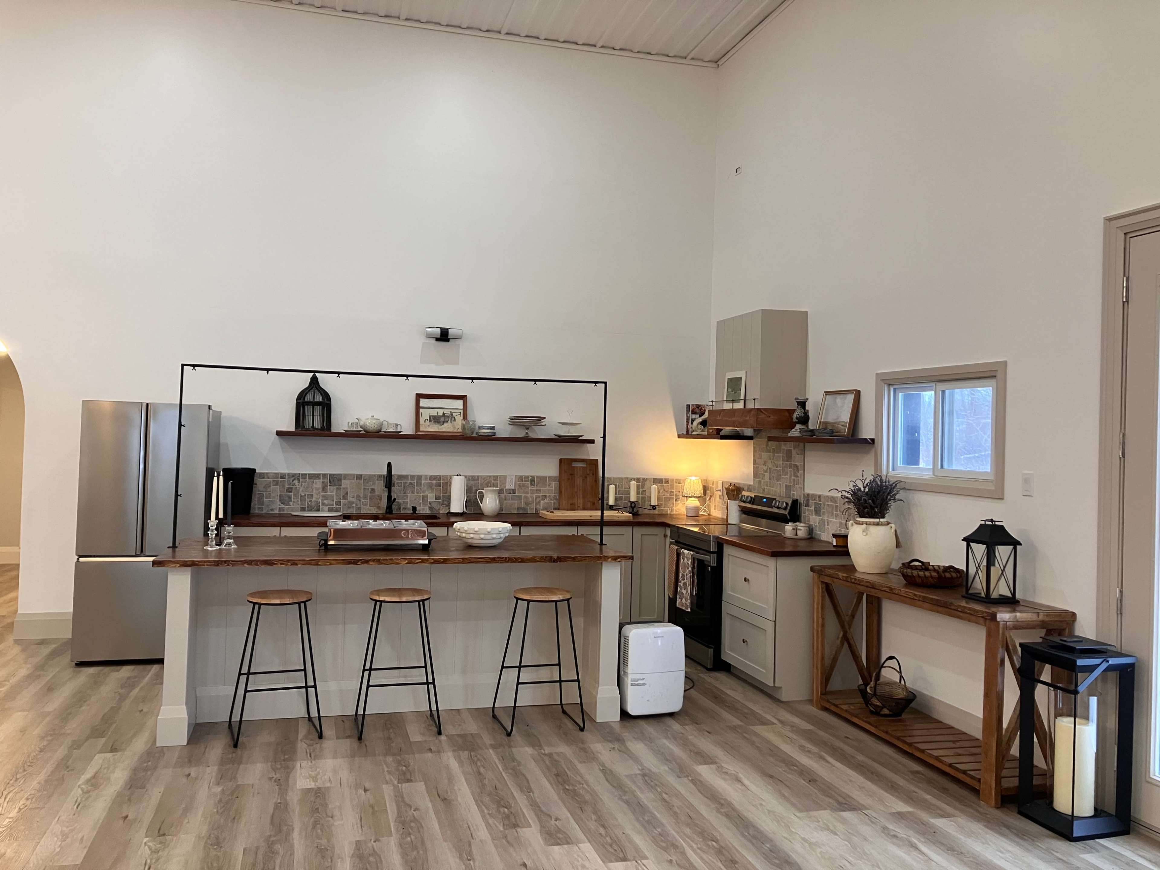 The image showcases a modern kitchen with a central island featuring three bar stools, equipped with stainless steel appliances and a mix of wooden and white cabinetry.