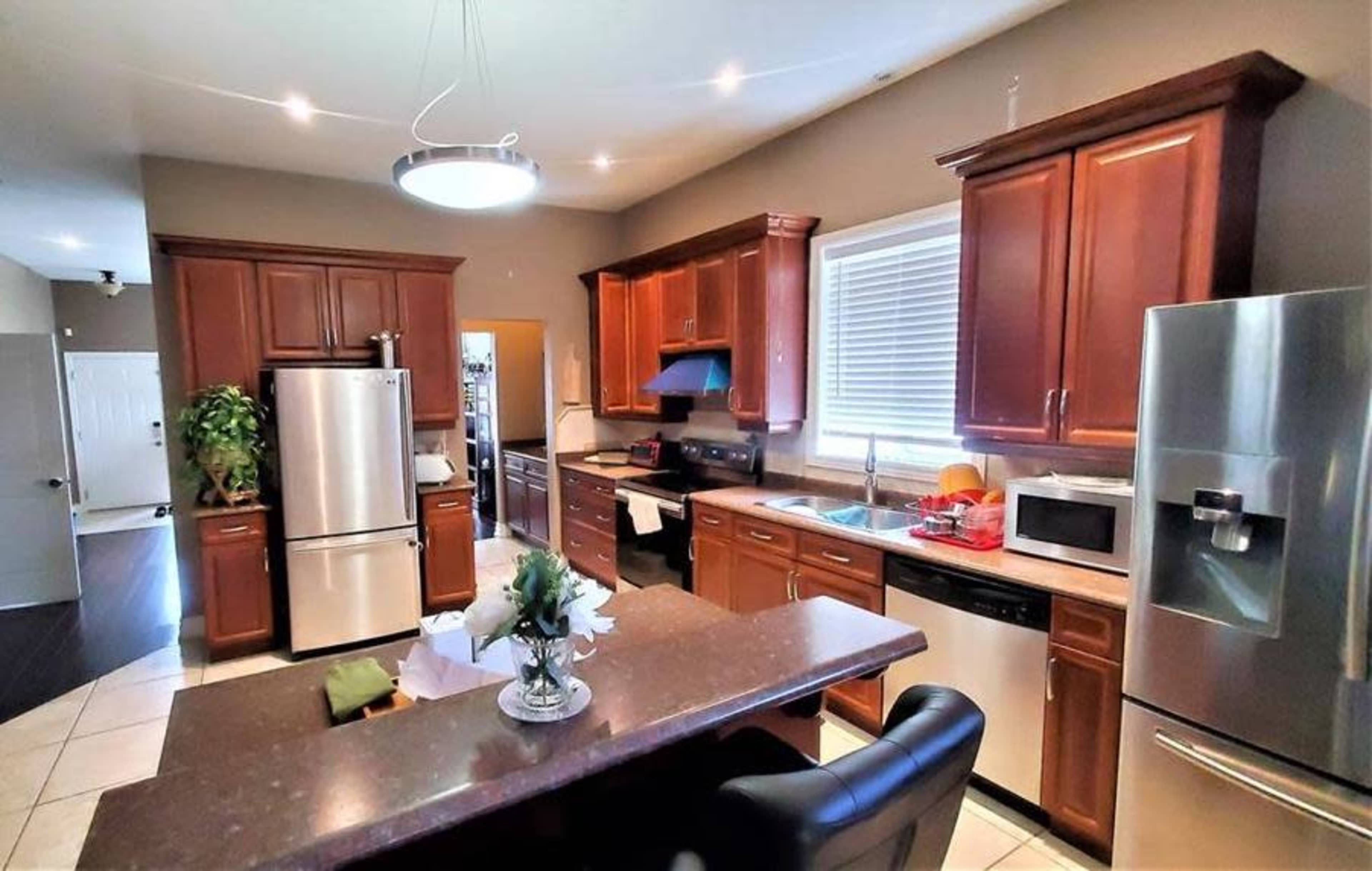 A modern kitchen with wooden cabinetry, stainless steel appliances, a central island, and a window with light streaming in.