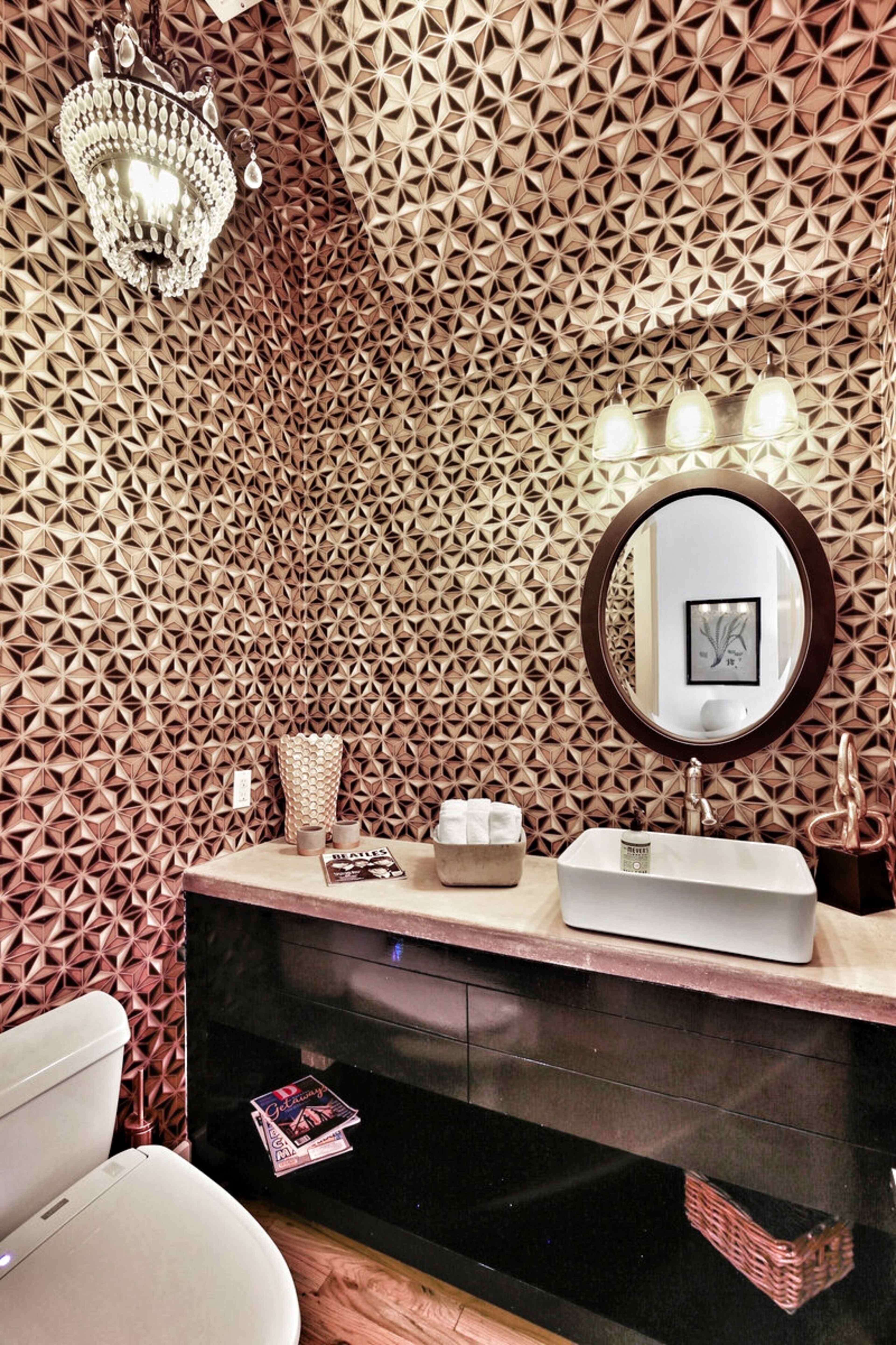 A modern bathroom featuring a geometric patterned wall, a countertop sink, a round mirror, and a chandelier.