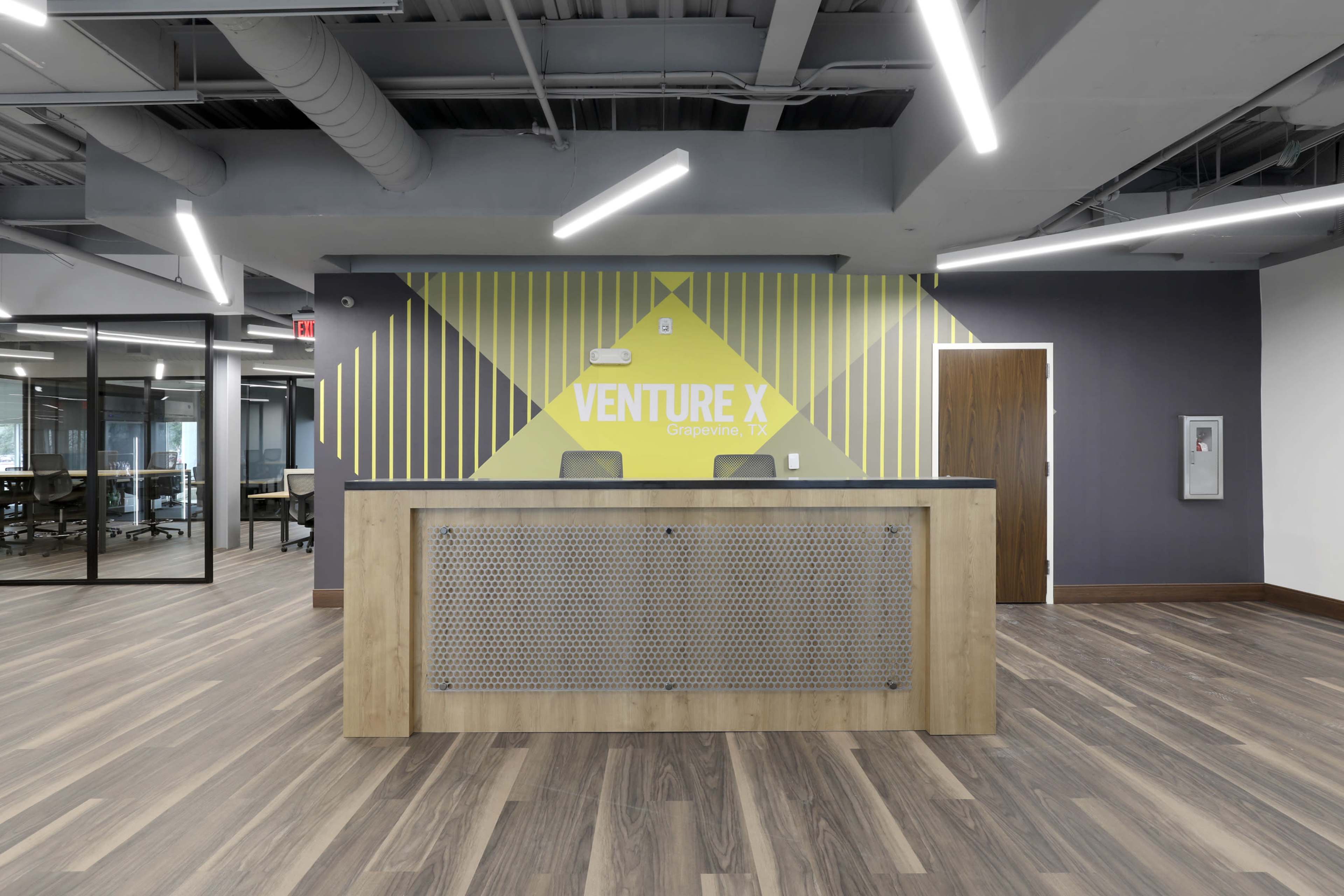 A modern reception area with a wooden front desk against a geometric patterned wall that features the text "VENTURE X."