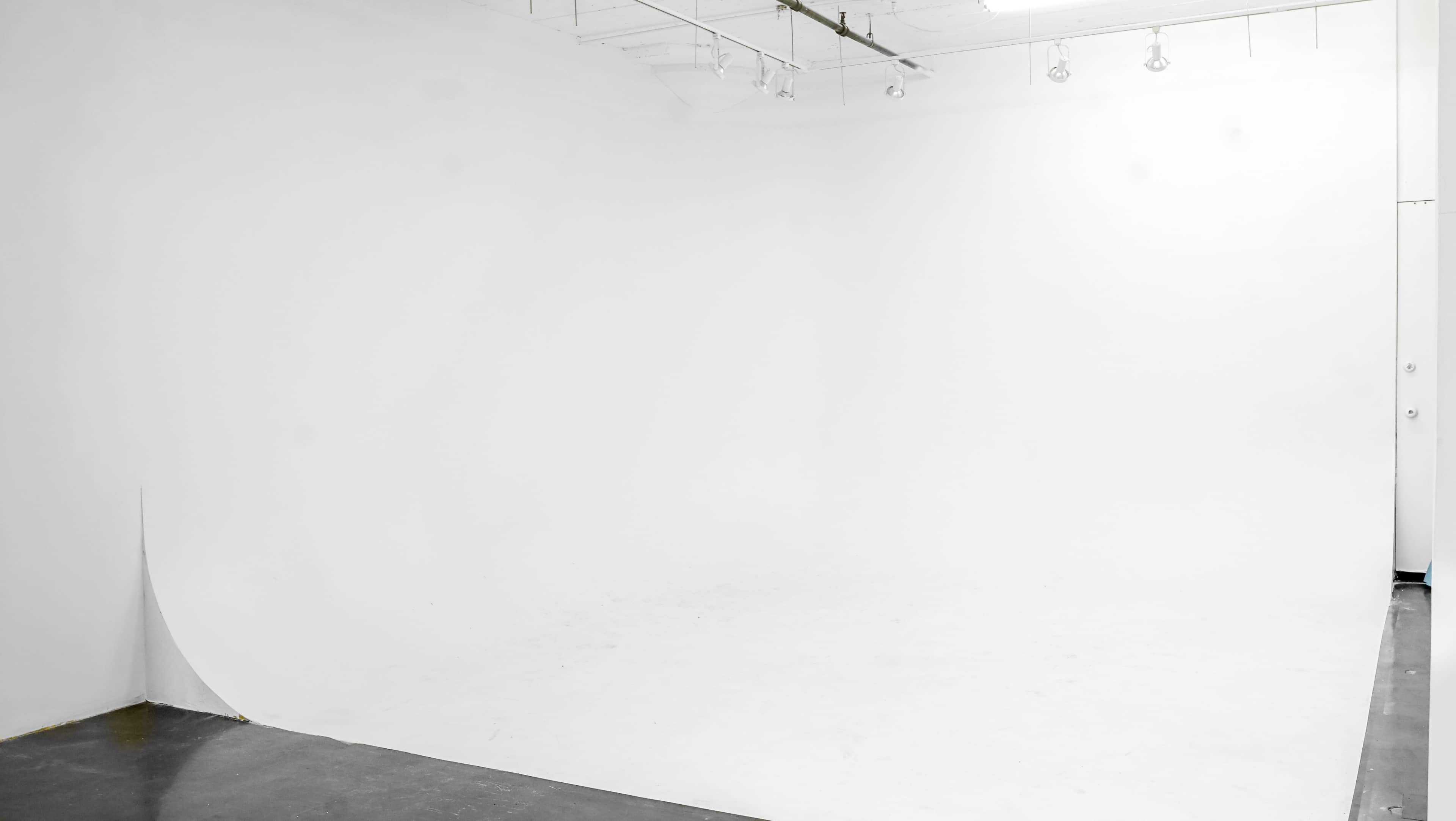 A spacious, empty studio with a white backdrop and polished floor.