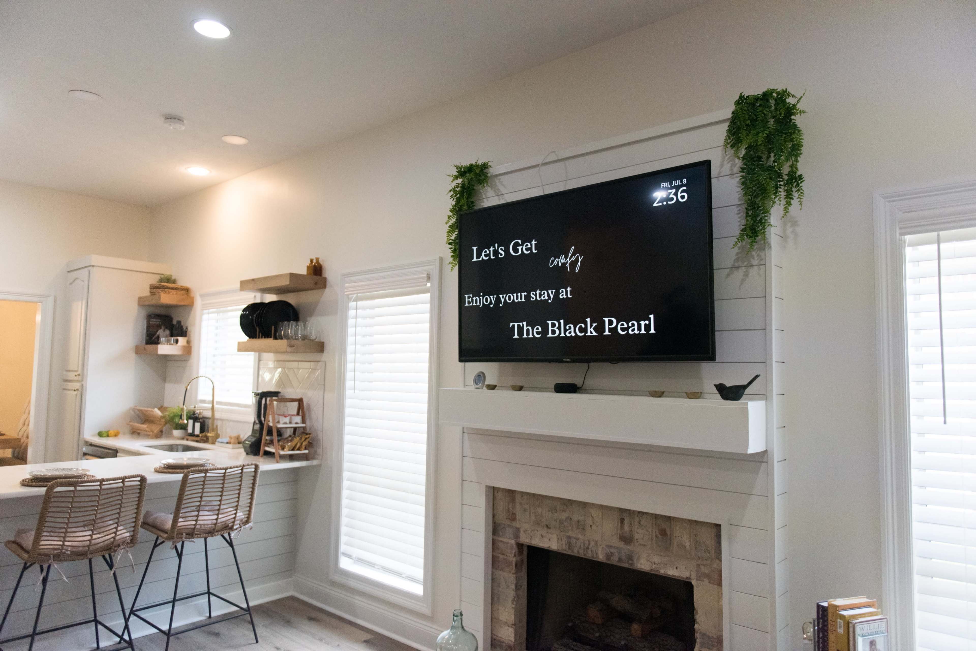 A living space with a television mounted above a fireplace, displaying a welcoming message for a place called "The Black Pearl."
