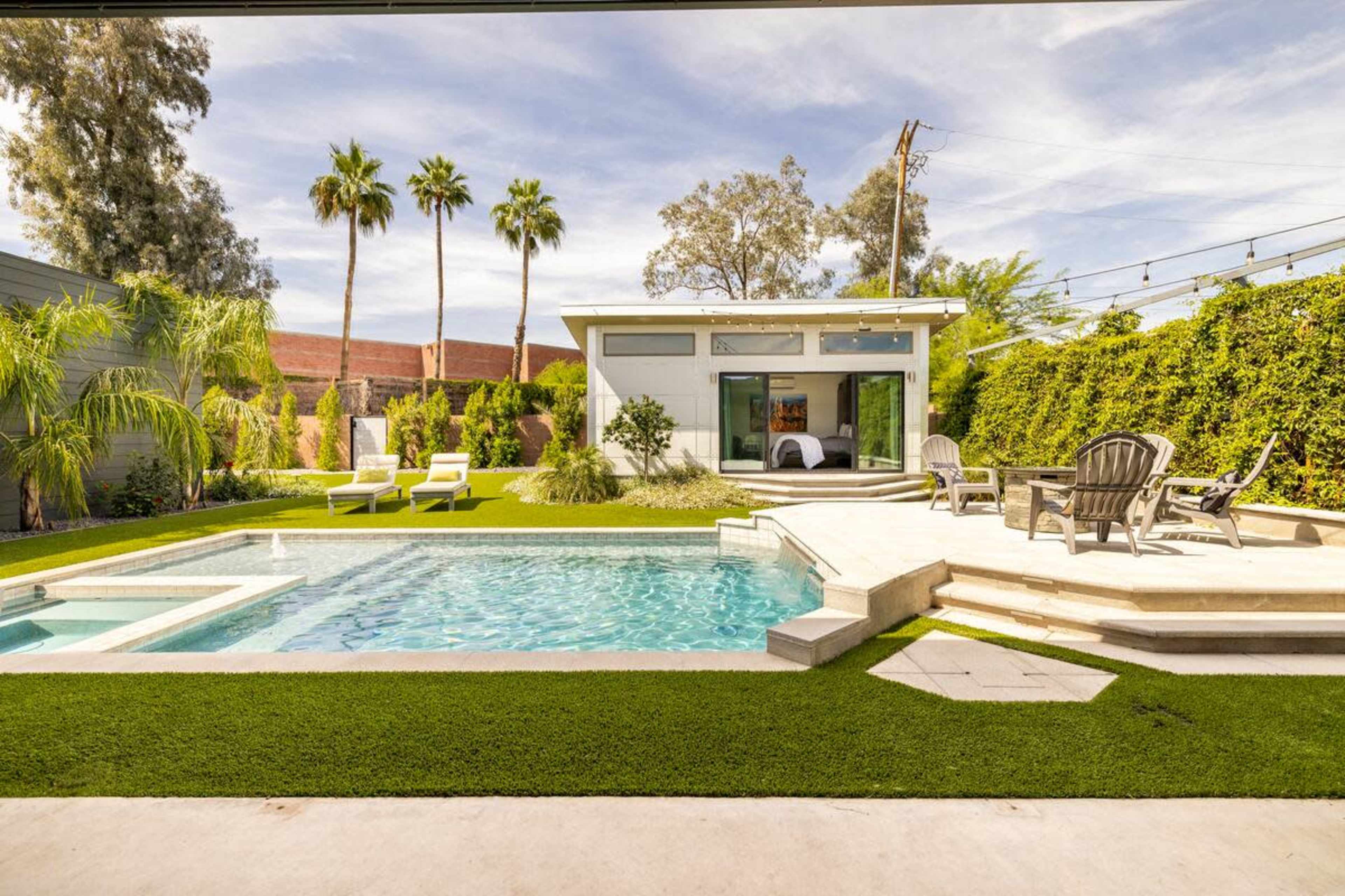 The image shows a modern backyard with a pool, lounge chairs, and palm trees, situated beside a contemporary house.