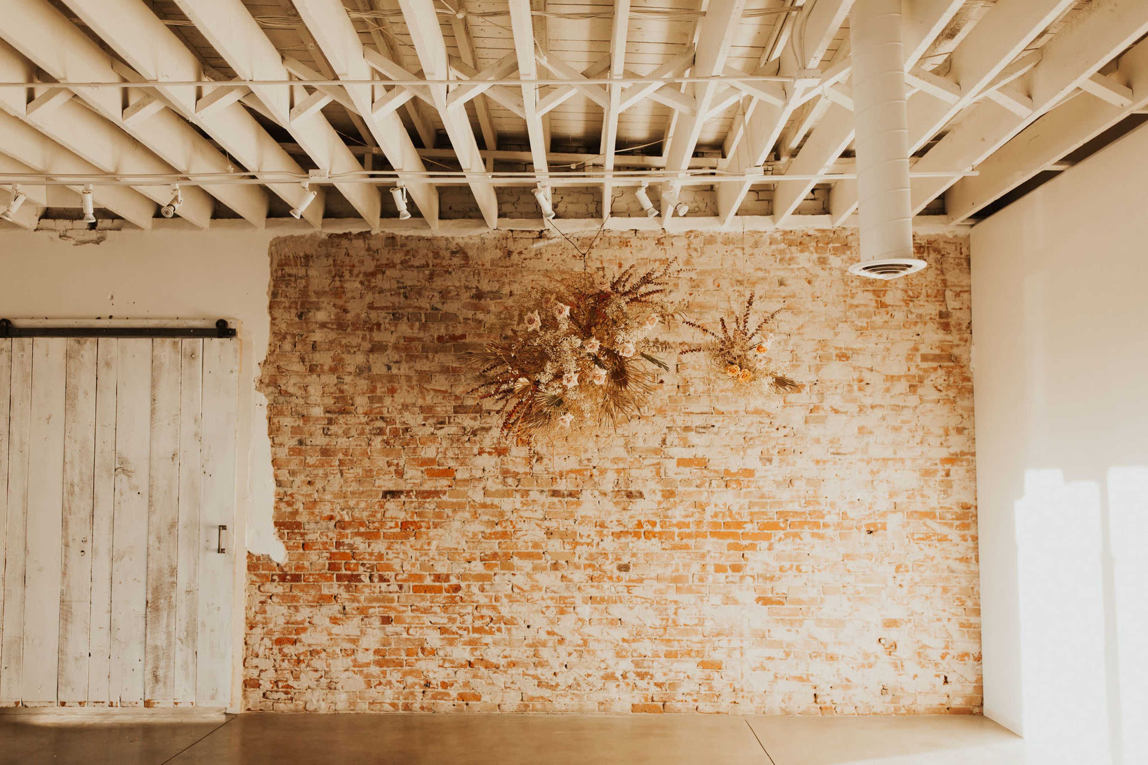 A rustic room with a brick wall, a white wooden sliding door, and dried floral arrangements hanging above.