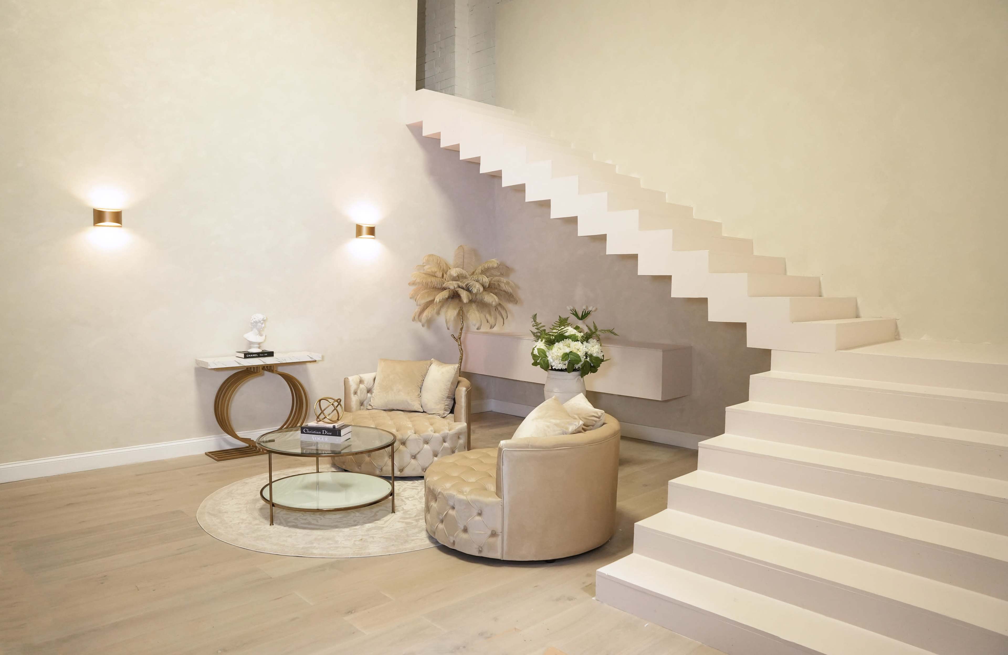 A modern interior features a light-colored room with a circular seating arrangement and a staircase leading to an upper level.