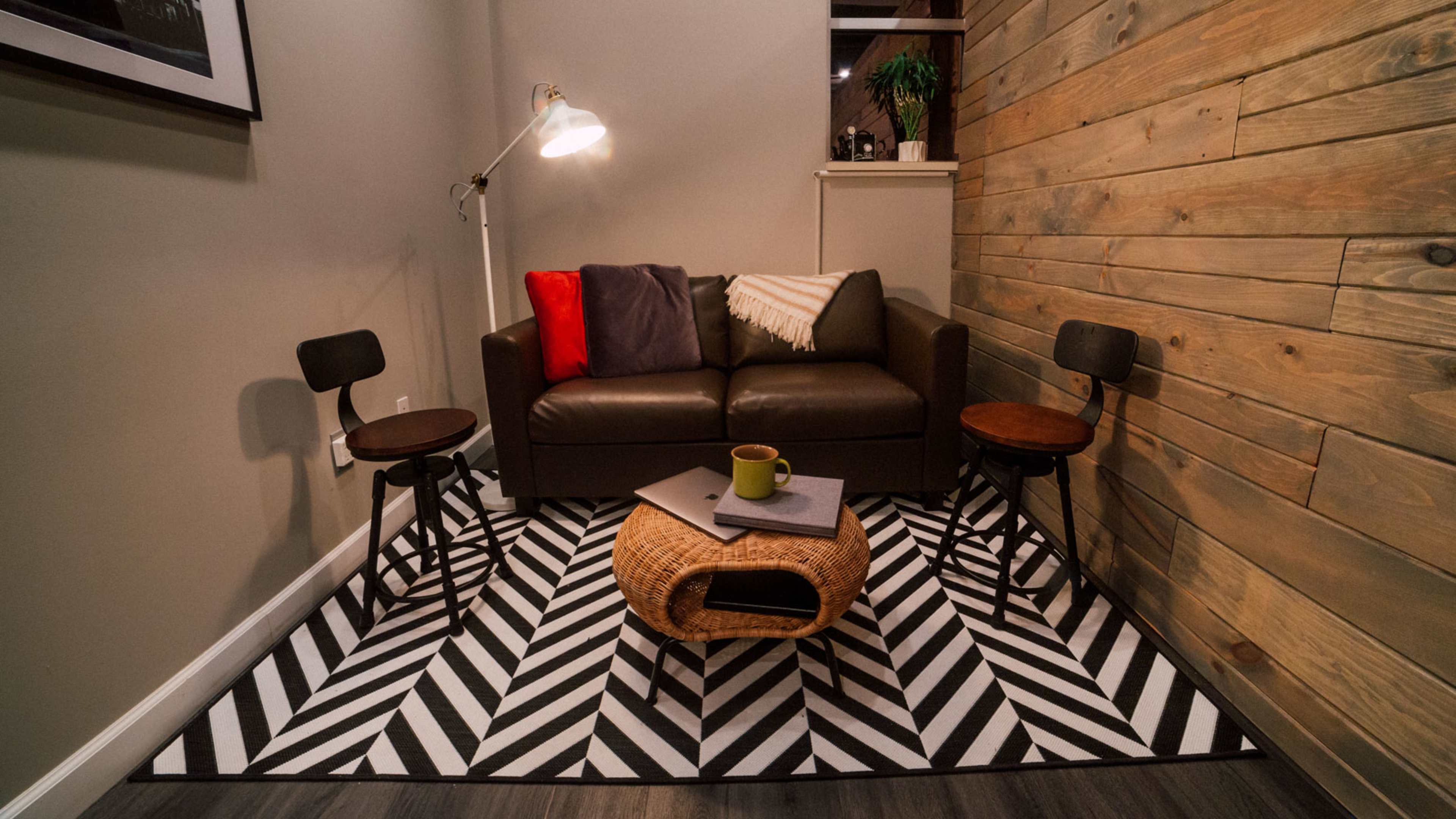 A small corner of a room featuring a brown sofa with a throw blanket, two round side tables, and a coffee table on a patterned rug.