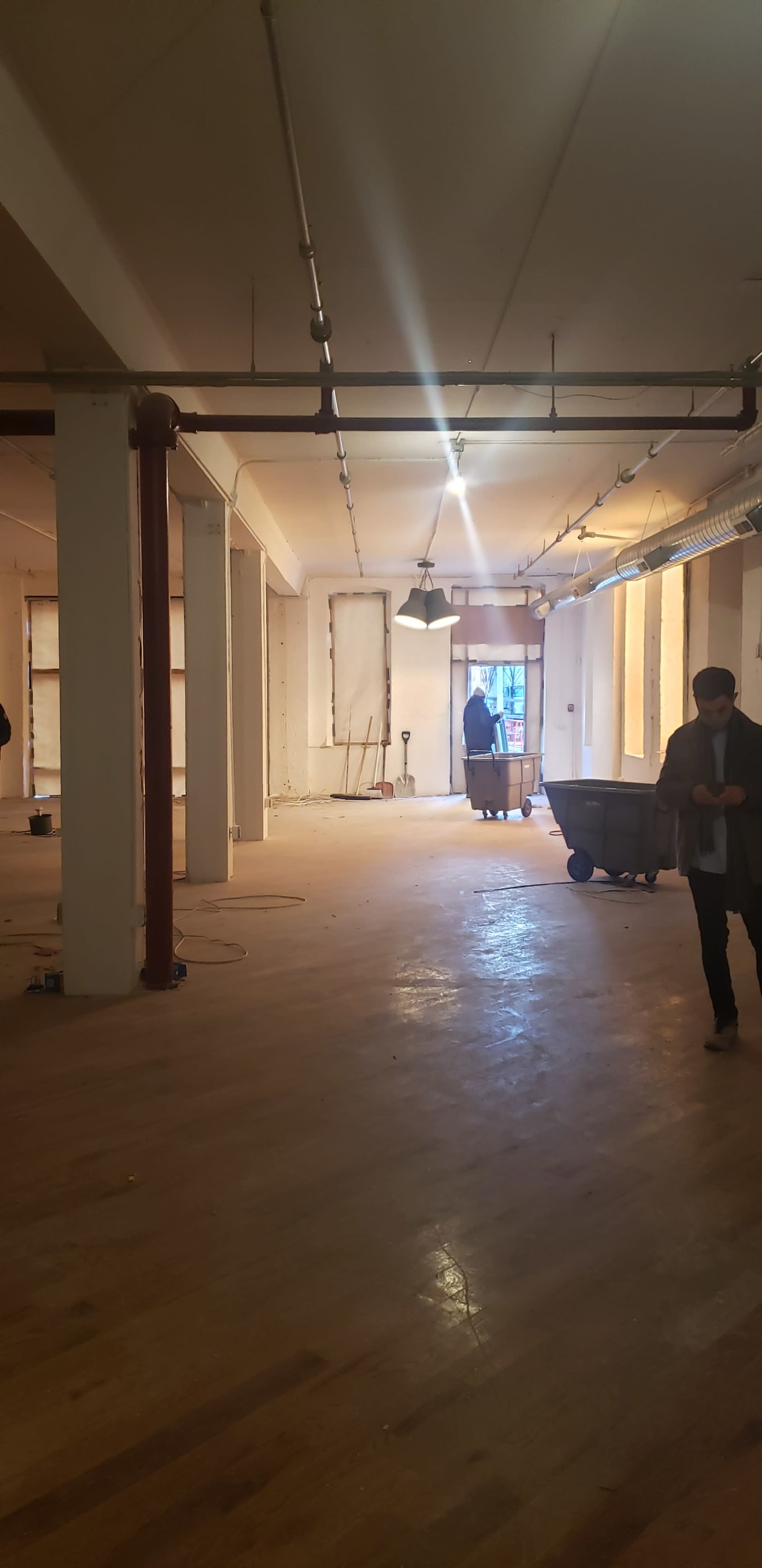 The image shows an unfinished interior space with wooden floors, exposed walls, and construction equipment scattered throughout.