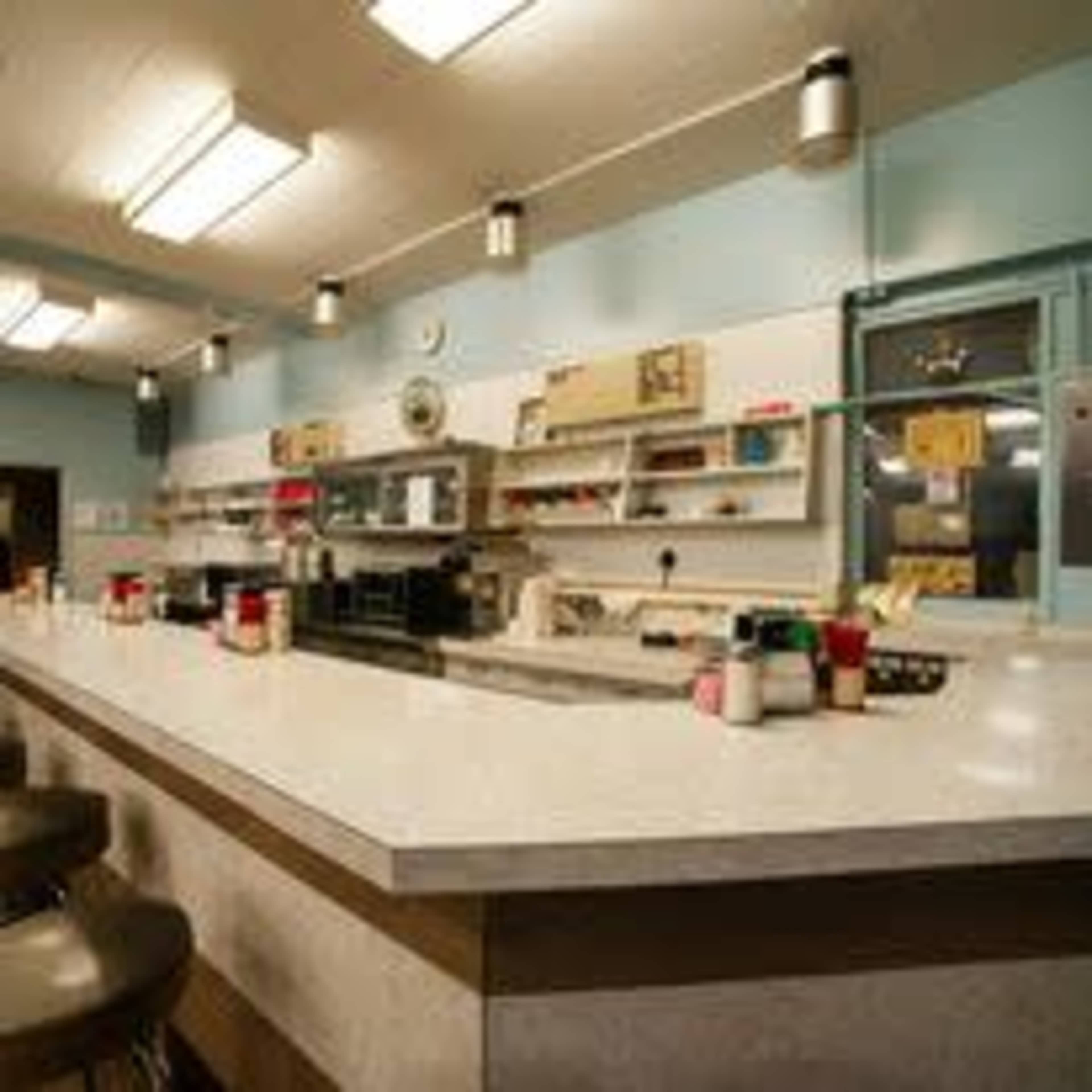 A retro diner counter with bar stools, a long marble surface, and shelves displaying various condiments and kitchen items against a blue wall.