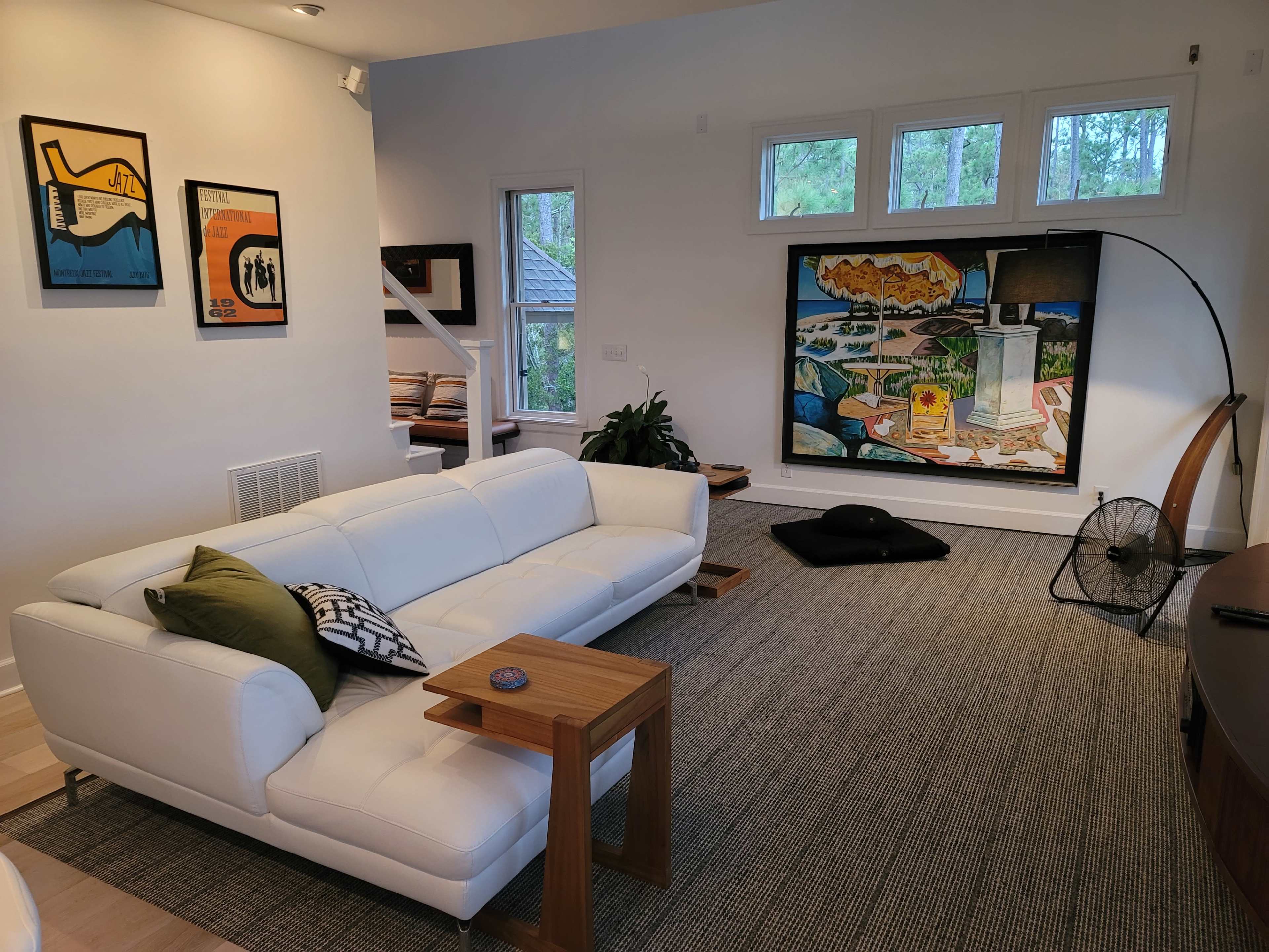 A bright living room with a white sofa, wooden side table, and a large colorful painting on the wall.