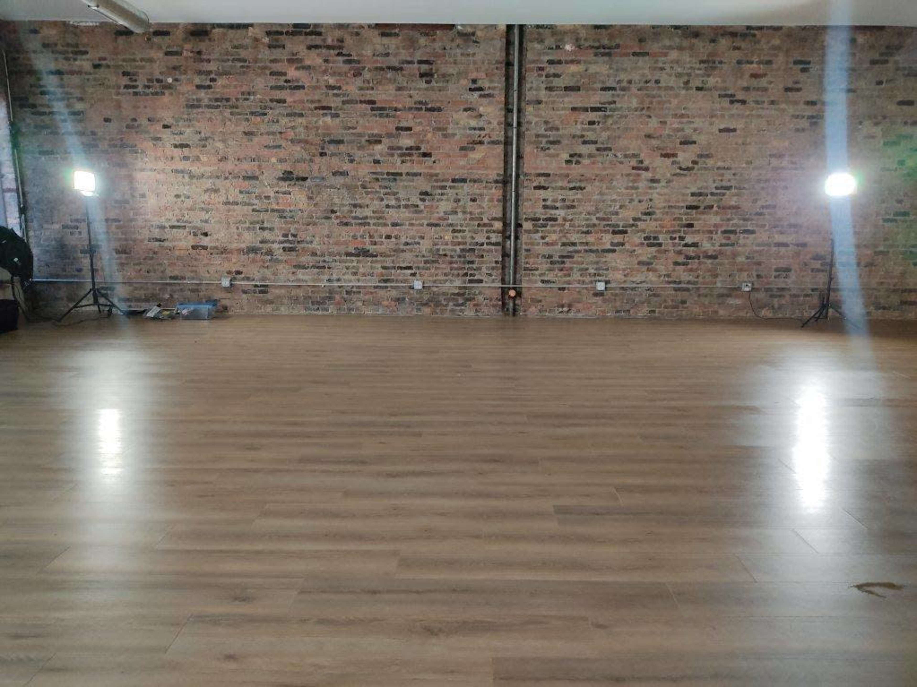 A spacious room features a wooden floor and exposed brick walls, illuminated by two standing lights.