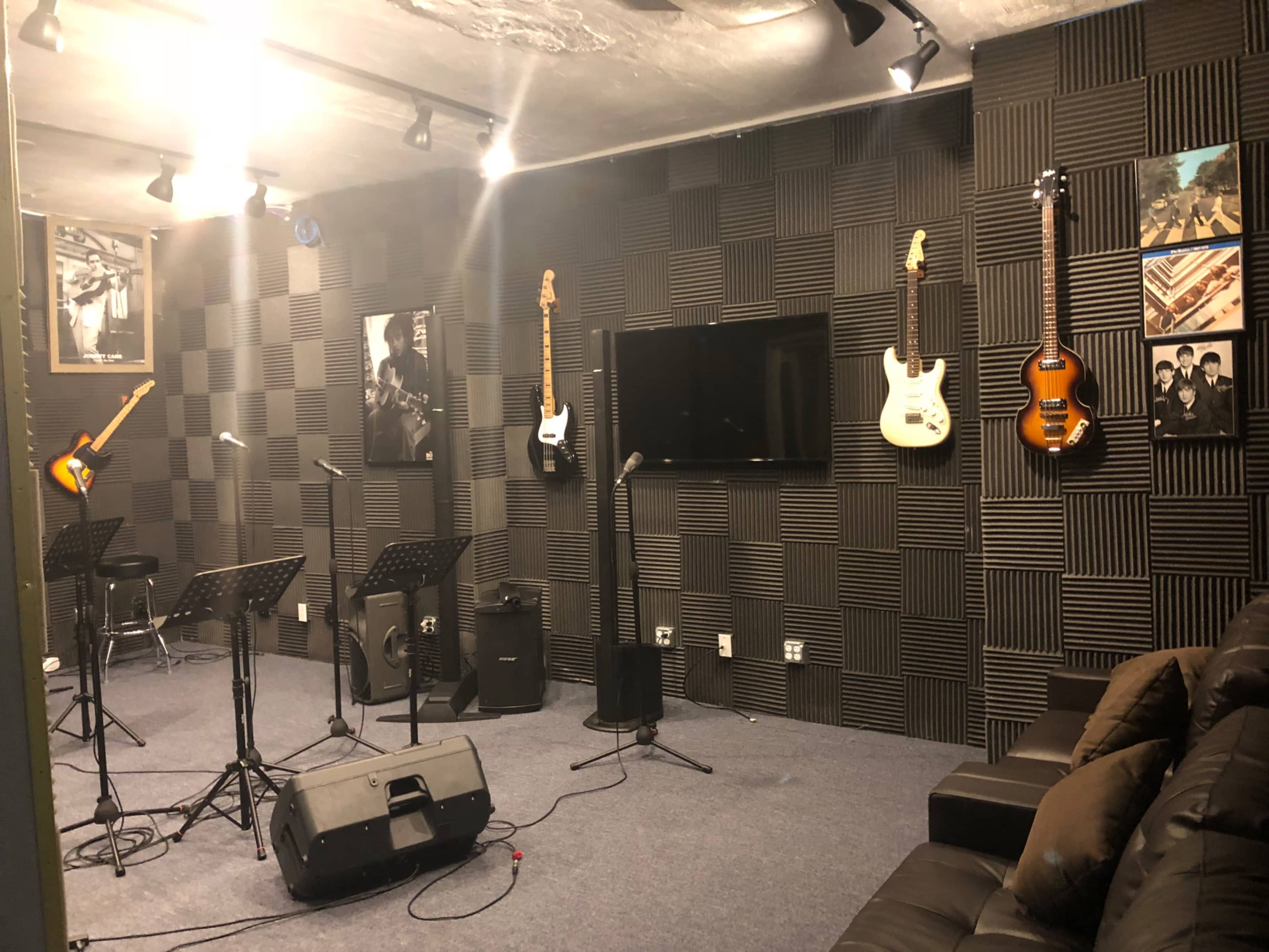 A music rehearsal space featuring electric guitars mounted on walls, soundproof foam panels, a television, and a black couch.