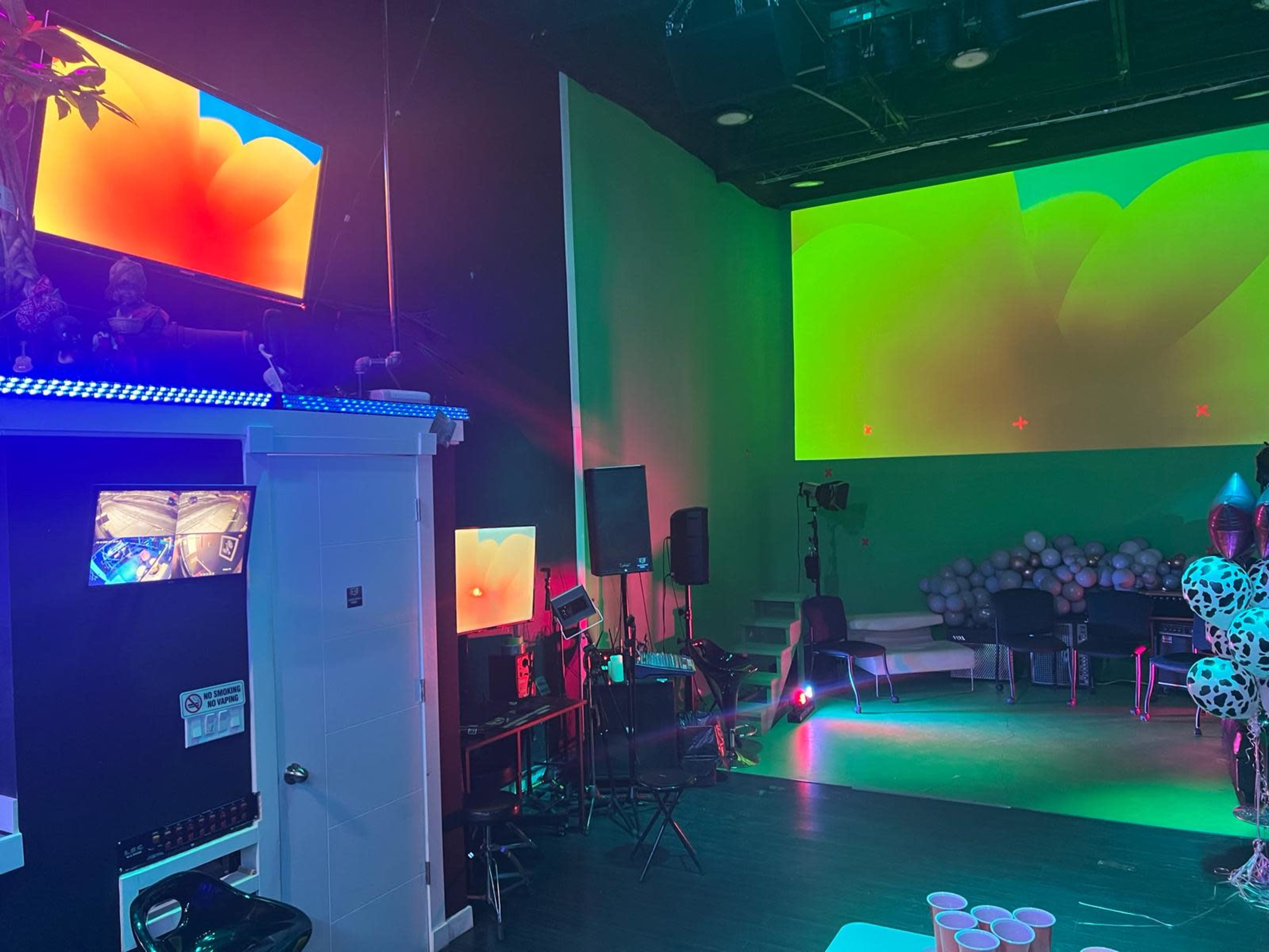 A brightly lit event space with colorful lighting, multiple screens displaying graphics, and chairs arranged for seating.