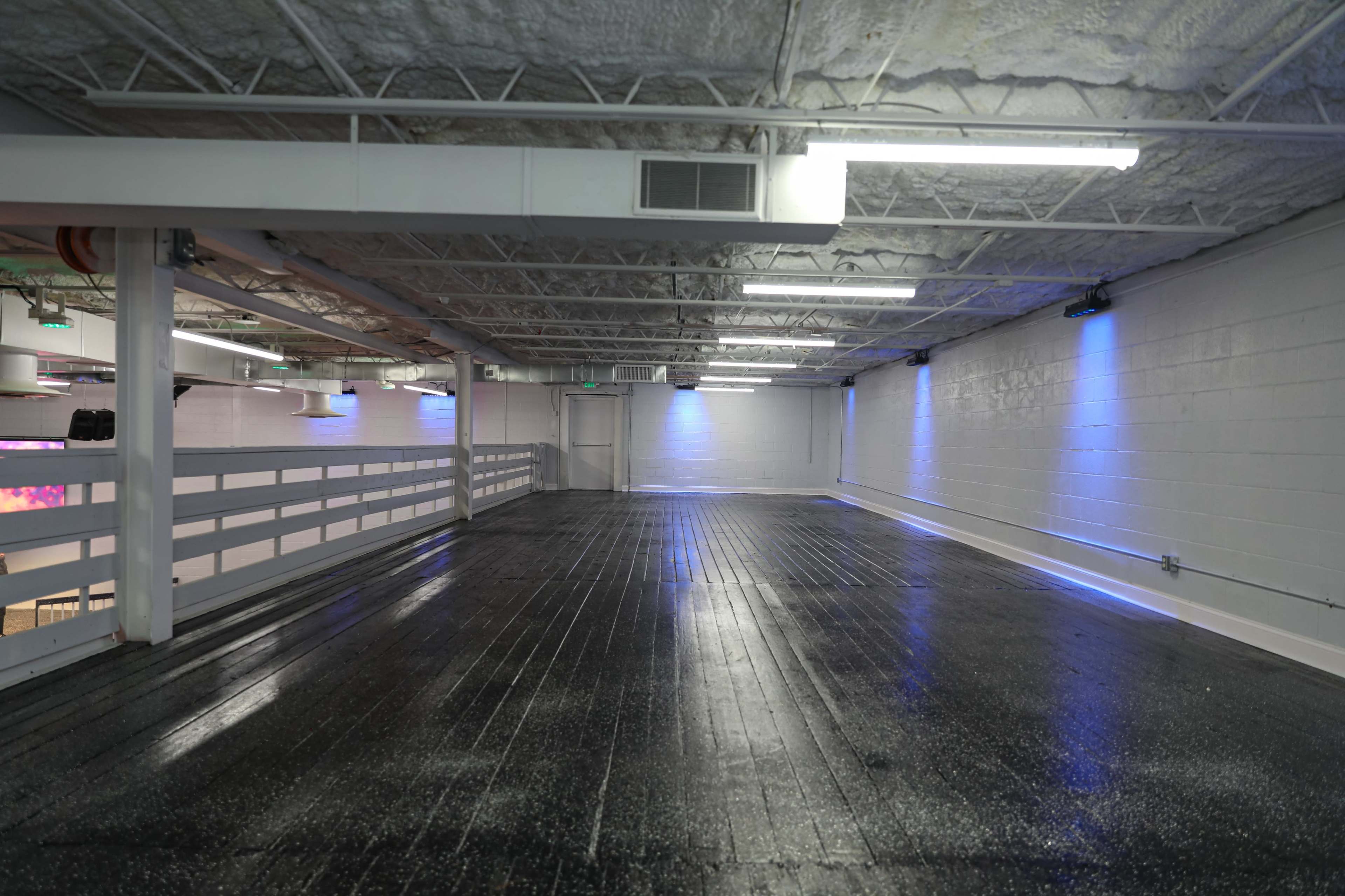 The image shows a spacious, mostly empty room with a polished black floor and dim blue lighting along the walls.