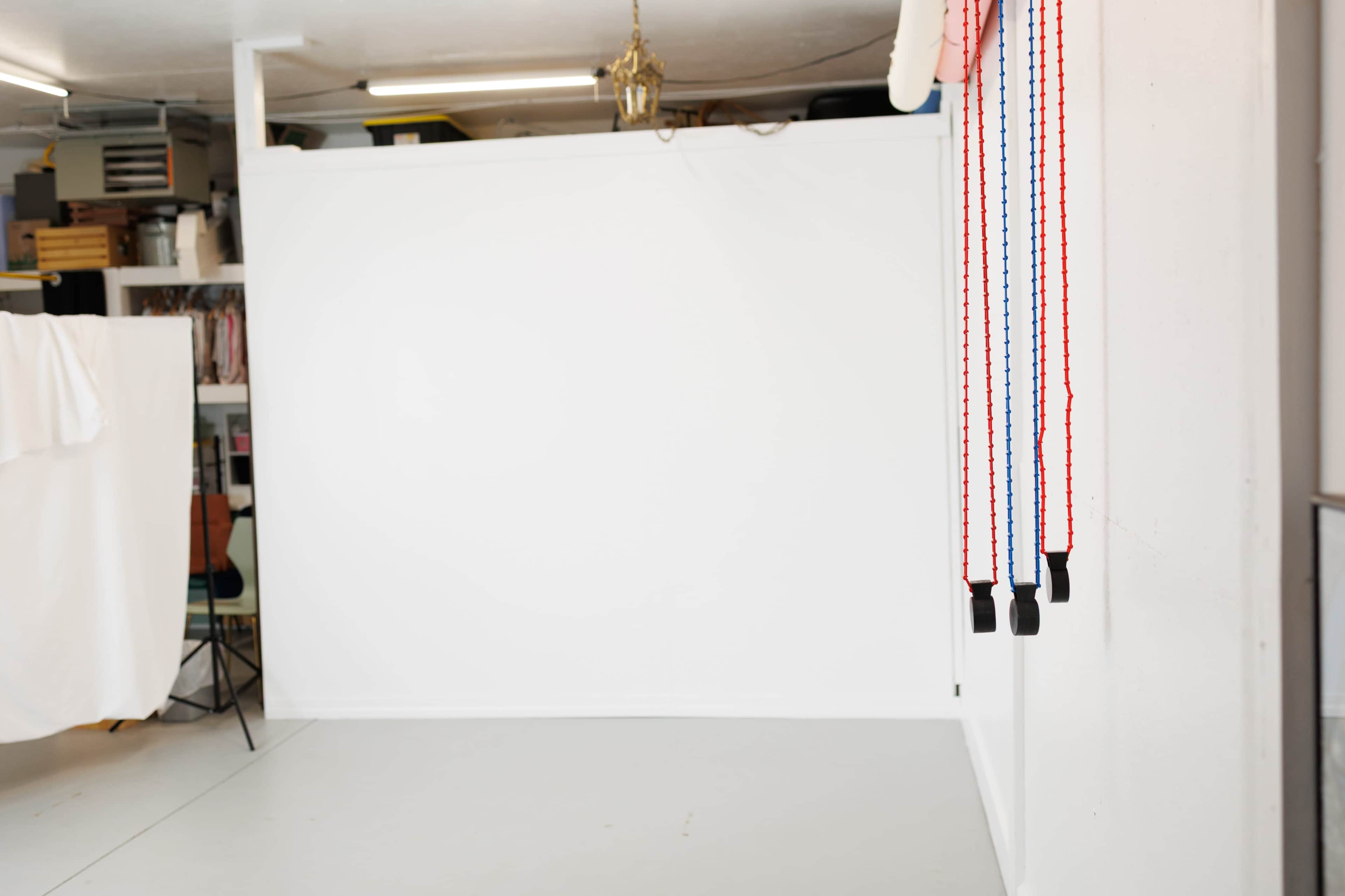 The image shows a spacious room with a plain white wall, a light-colored floor, and two colored straps hanging from the wall.