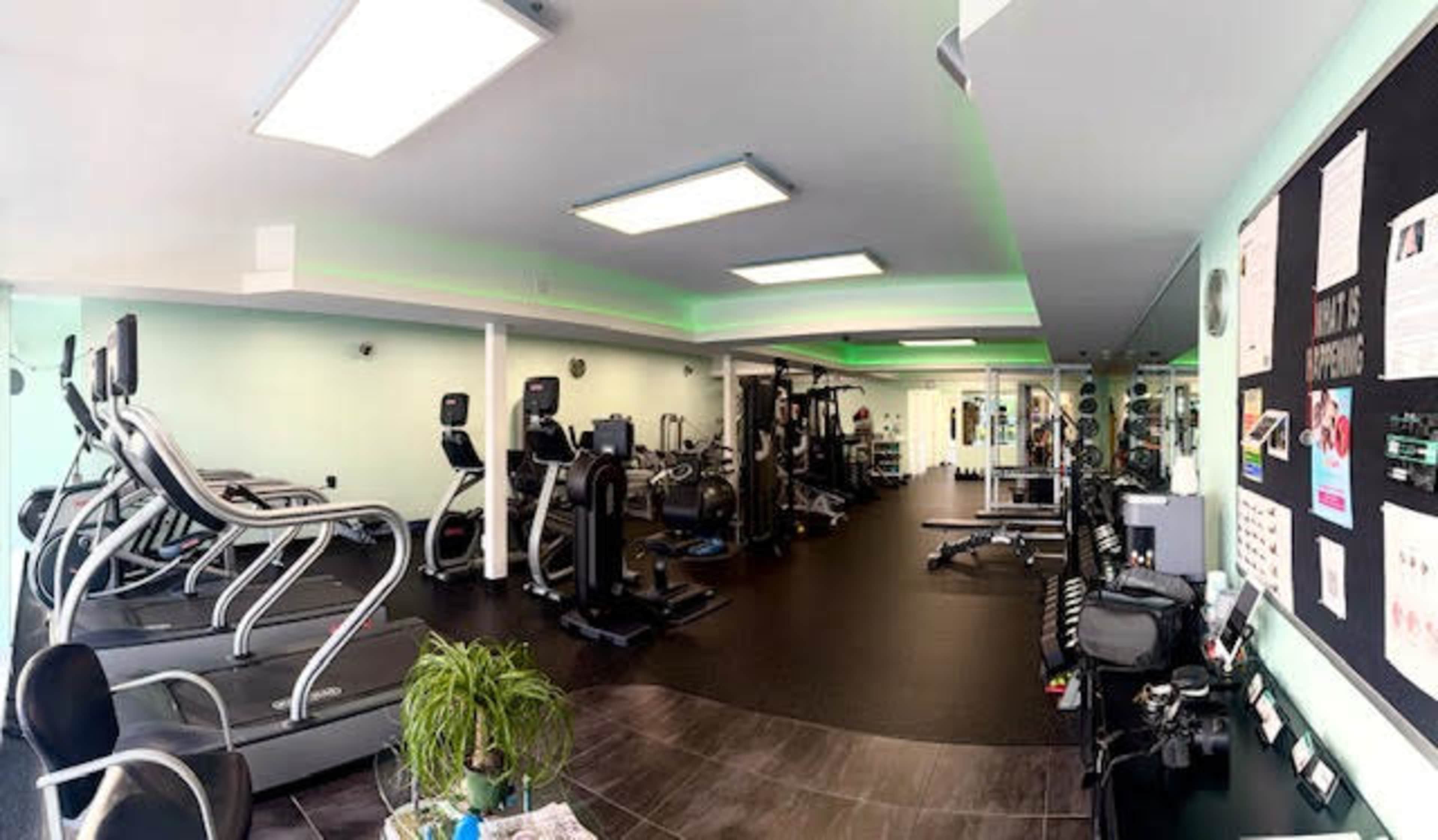 The image shows a modern gym interior with various exercise machines arranged neatly in a well-lit space.