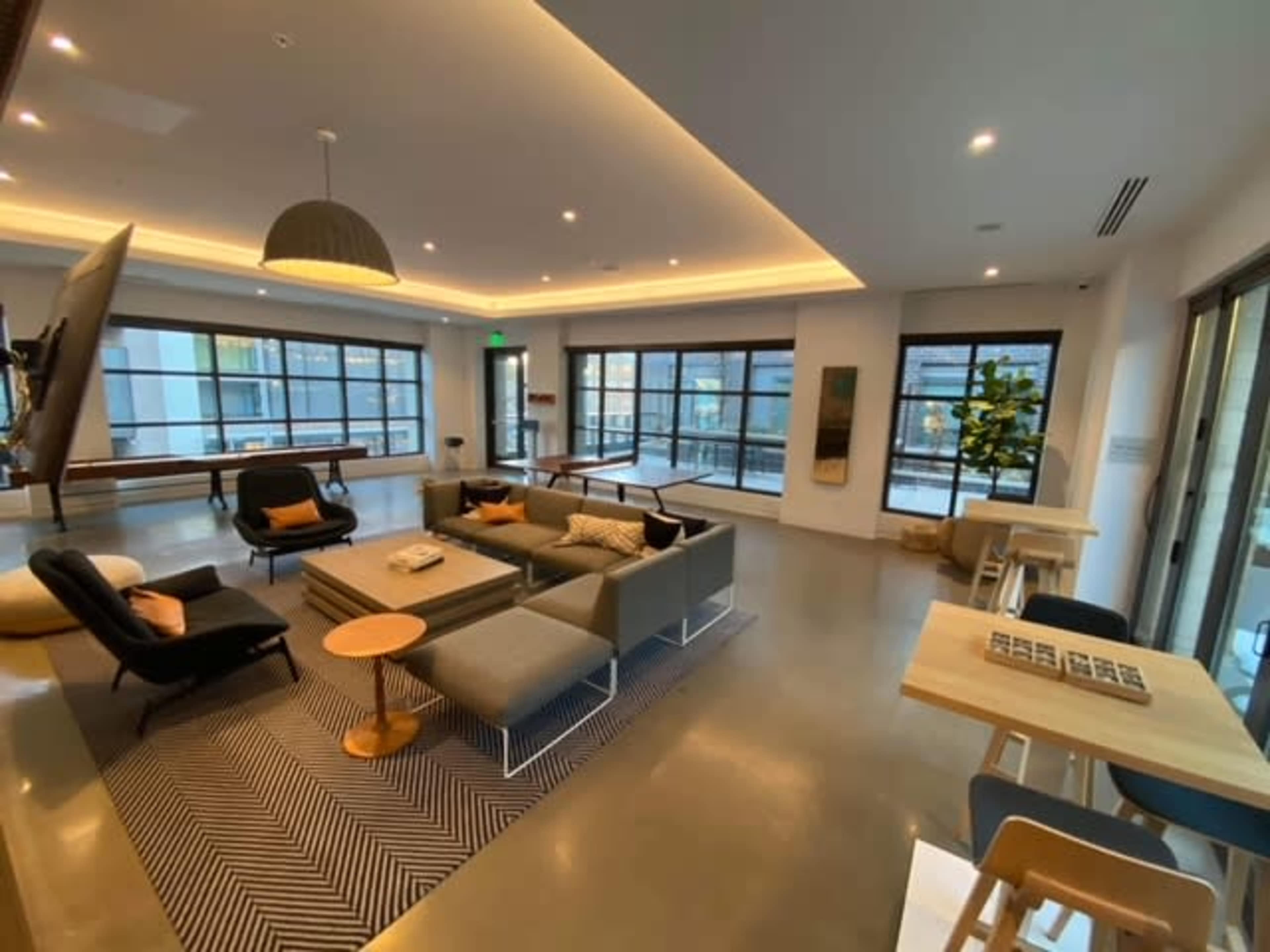 A modern lounge area with a gray sectional sofa, a round coffee table, and large windows allowing natural light to fill the space.