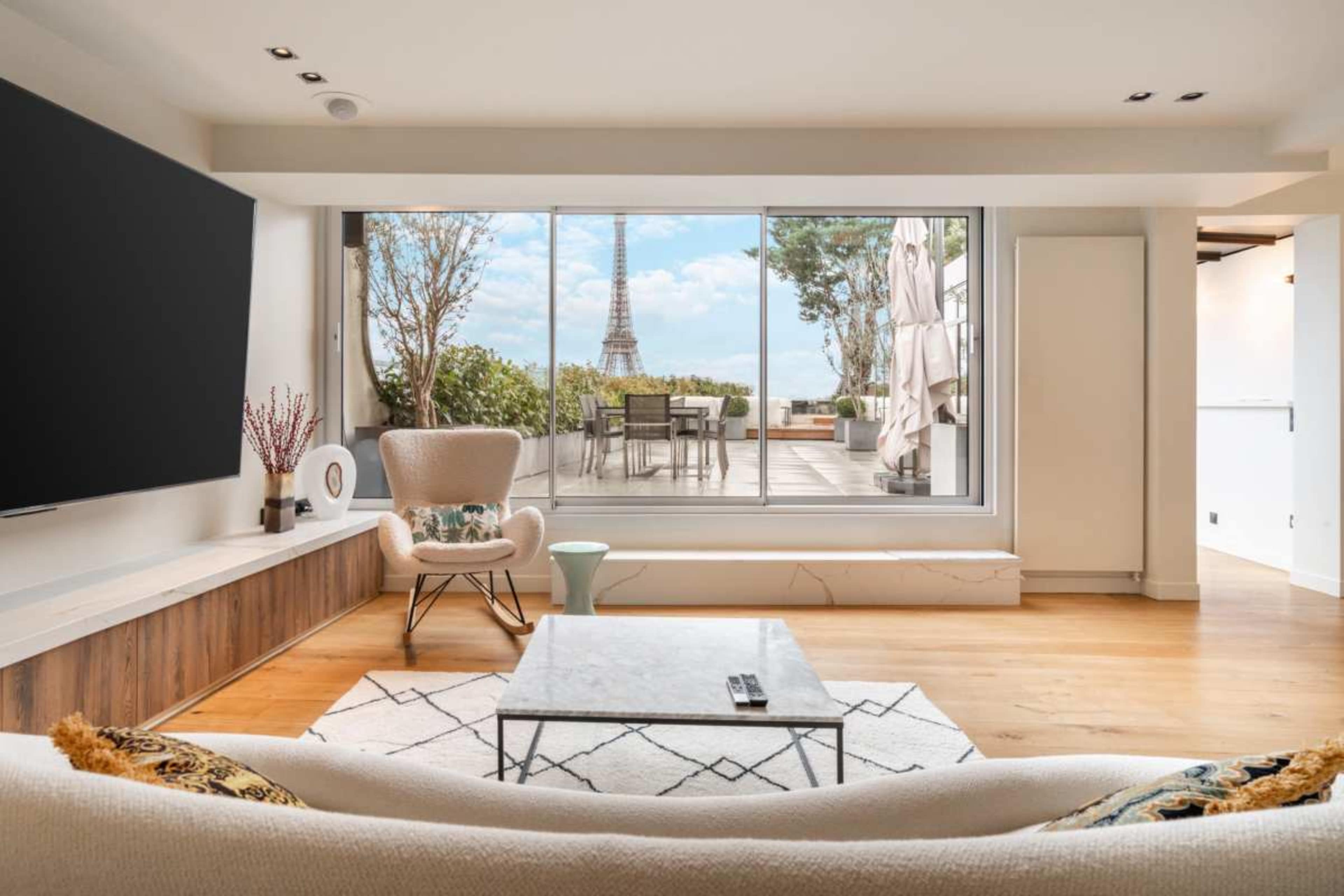 A modern living room features a large window with a view of the Eiffel Tower, complemented by stylish furniture and a coffee table.