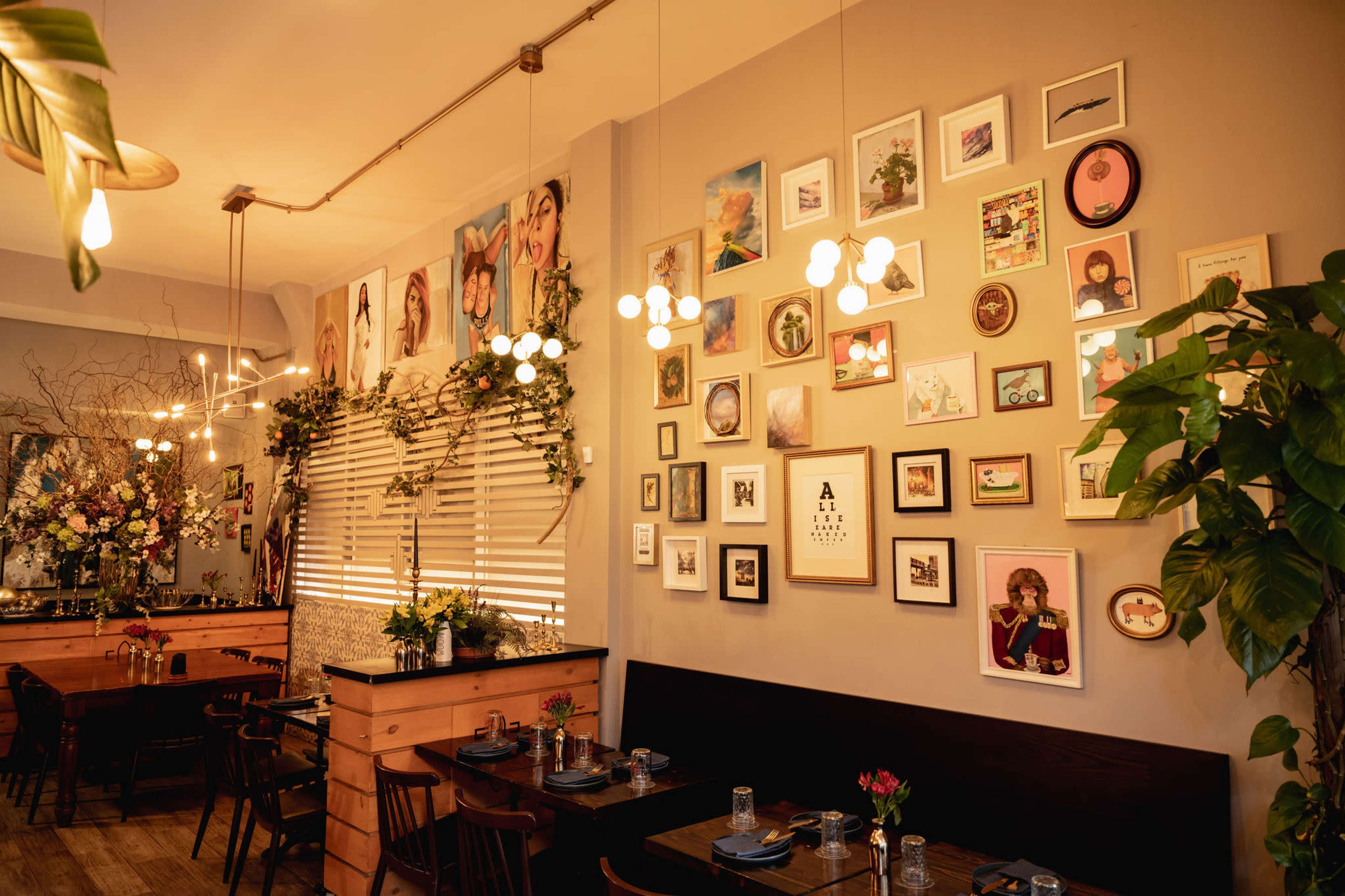 The interior of a restaurant features a wall adorned with various framed pictures, decorative plants, and modern light fixtures.