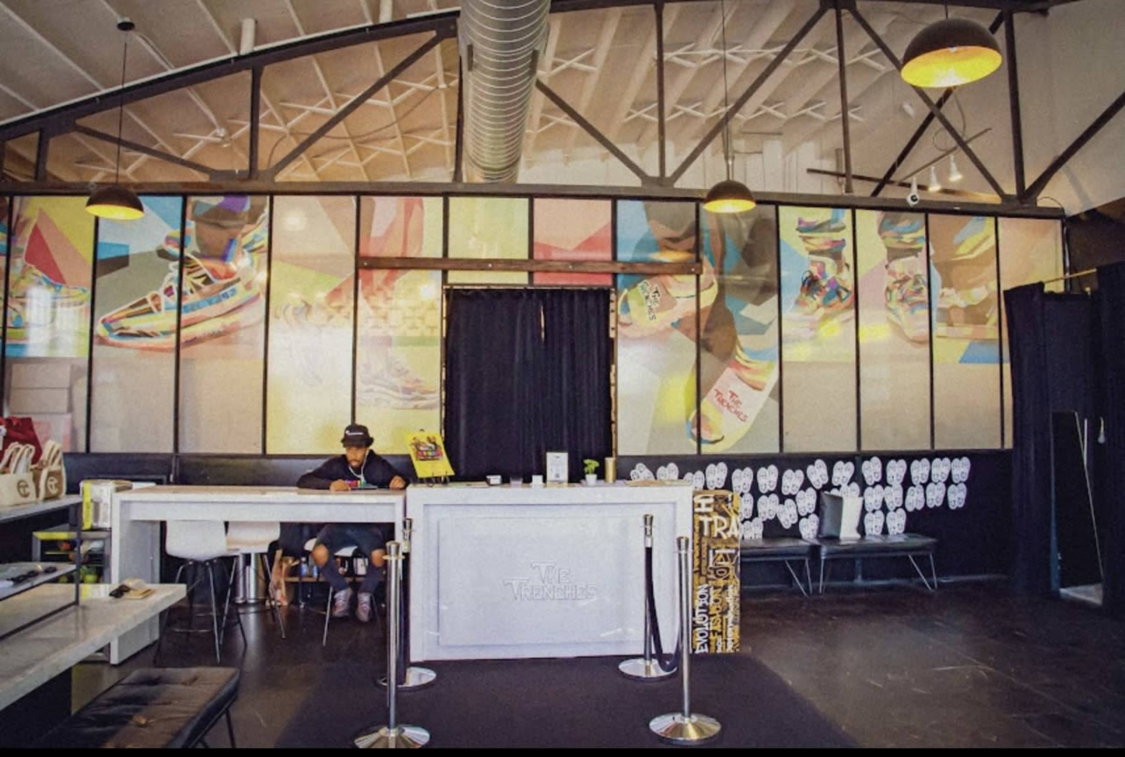 A man sits at a white reception desk in a modern space with colorful wall art and displays of merchandise.