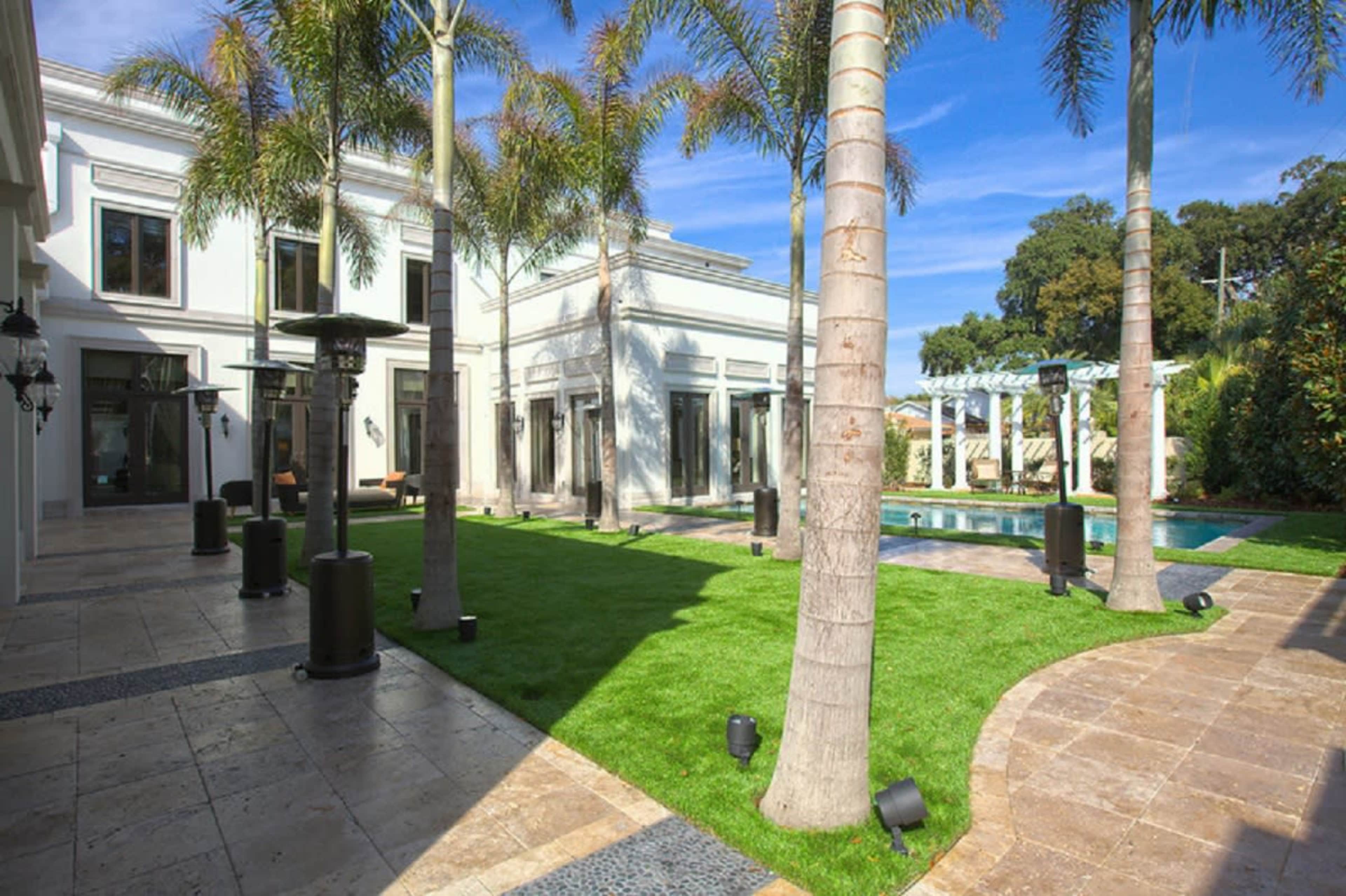A well-maintained courtyard featuring a manicured lawn, palm trees, stone pathways, and a swimming pool.