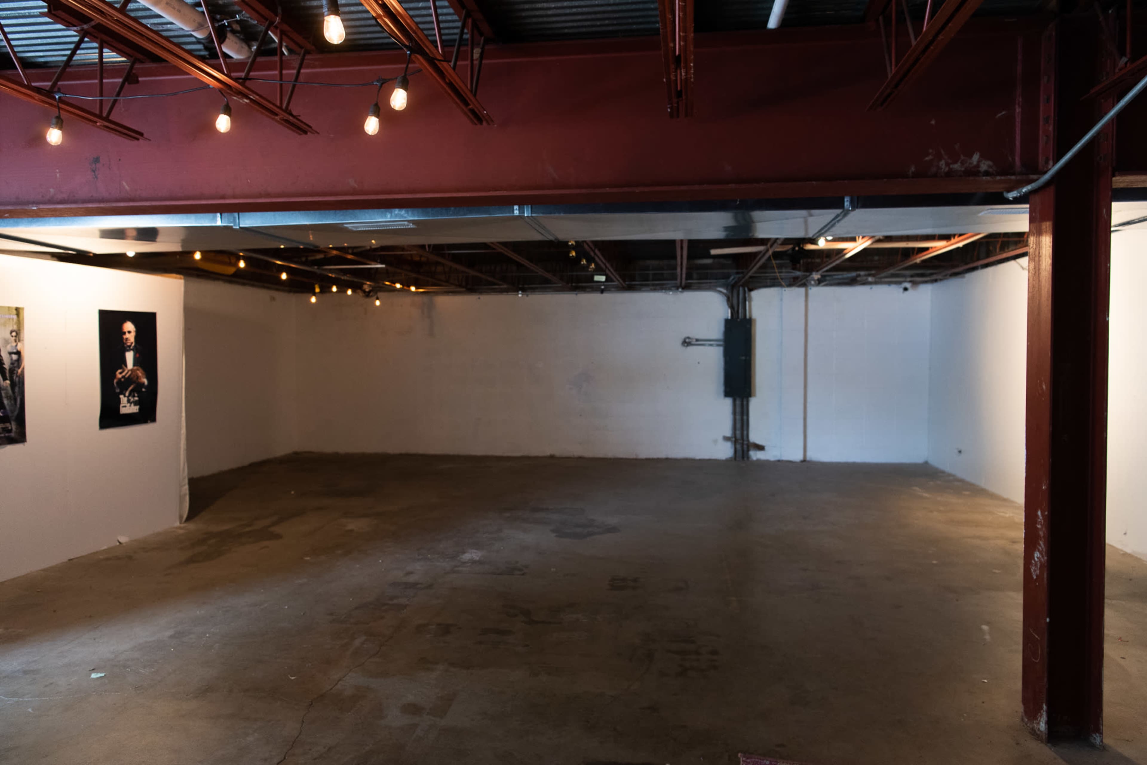 An empty industrial space with exposed beams, concrete flooring, and a few hanging light bulbs.