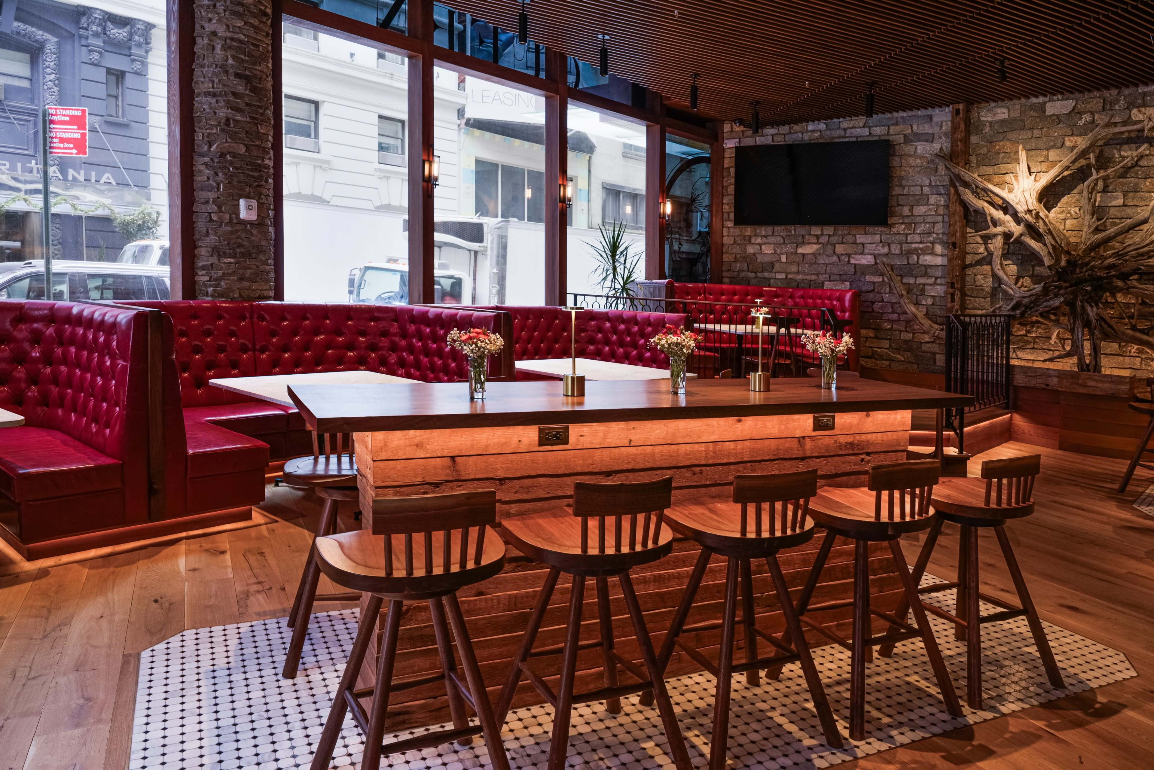 The image shows a modern restaurant interior with red upholstered seating, a large wooden table, and bar stools.