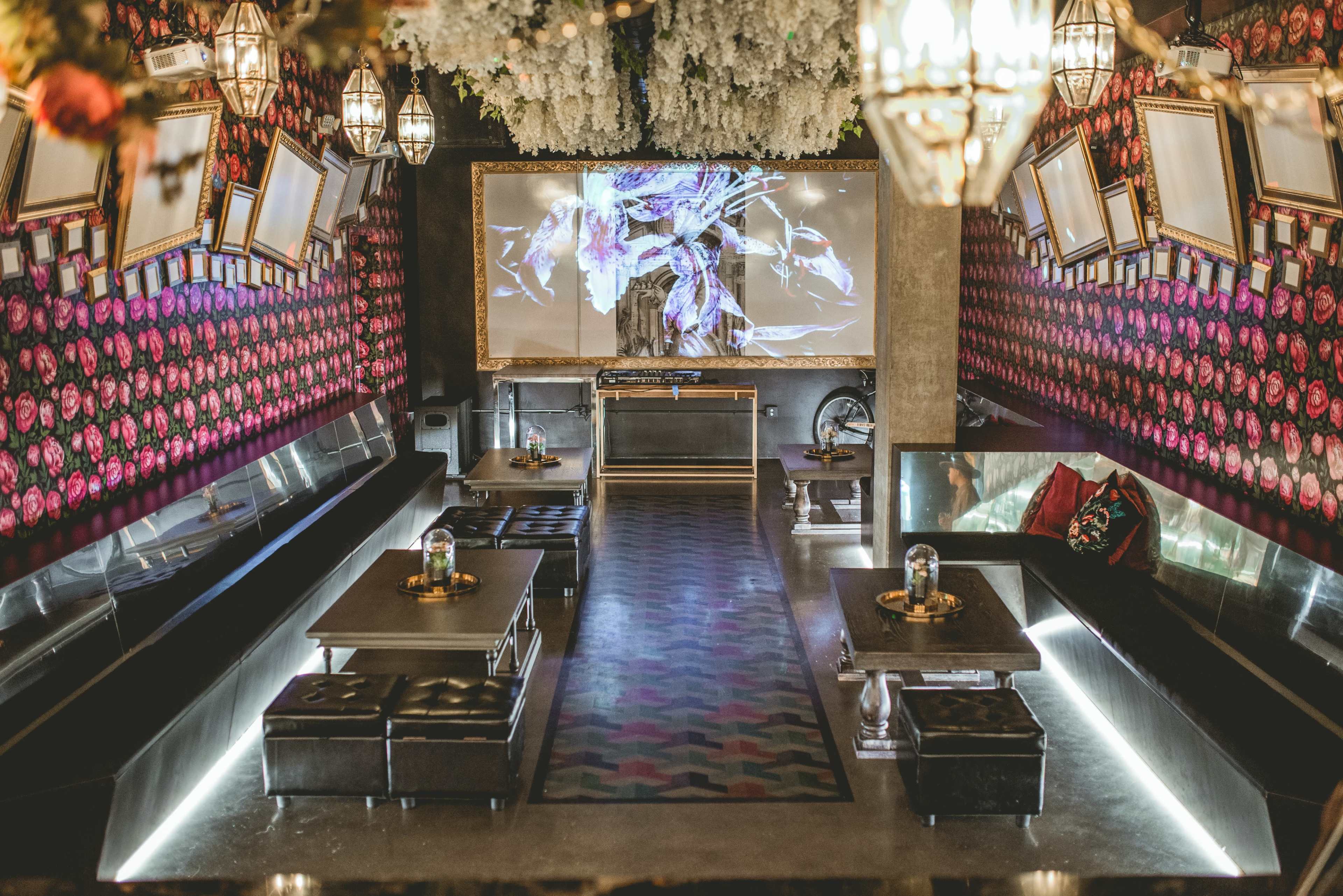 A modern restaurant with floral wallpaper, mirrored walls, low seating, and a central projection screen.