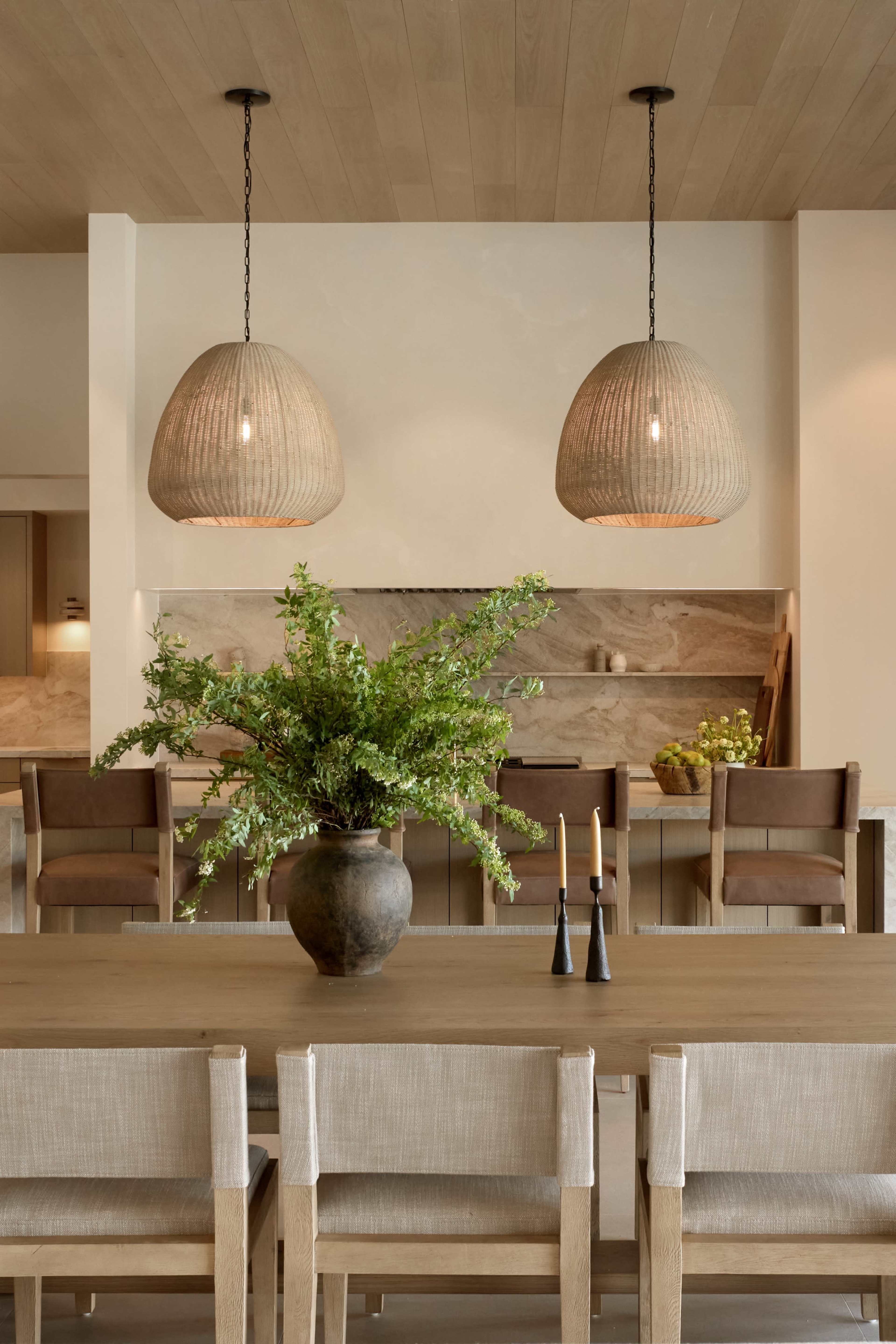 The image features a modern dining area with two large woven pendant lights above a wooden table, surrounded by chairs and a decorative vase filled with greenery.
