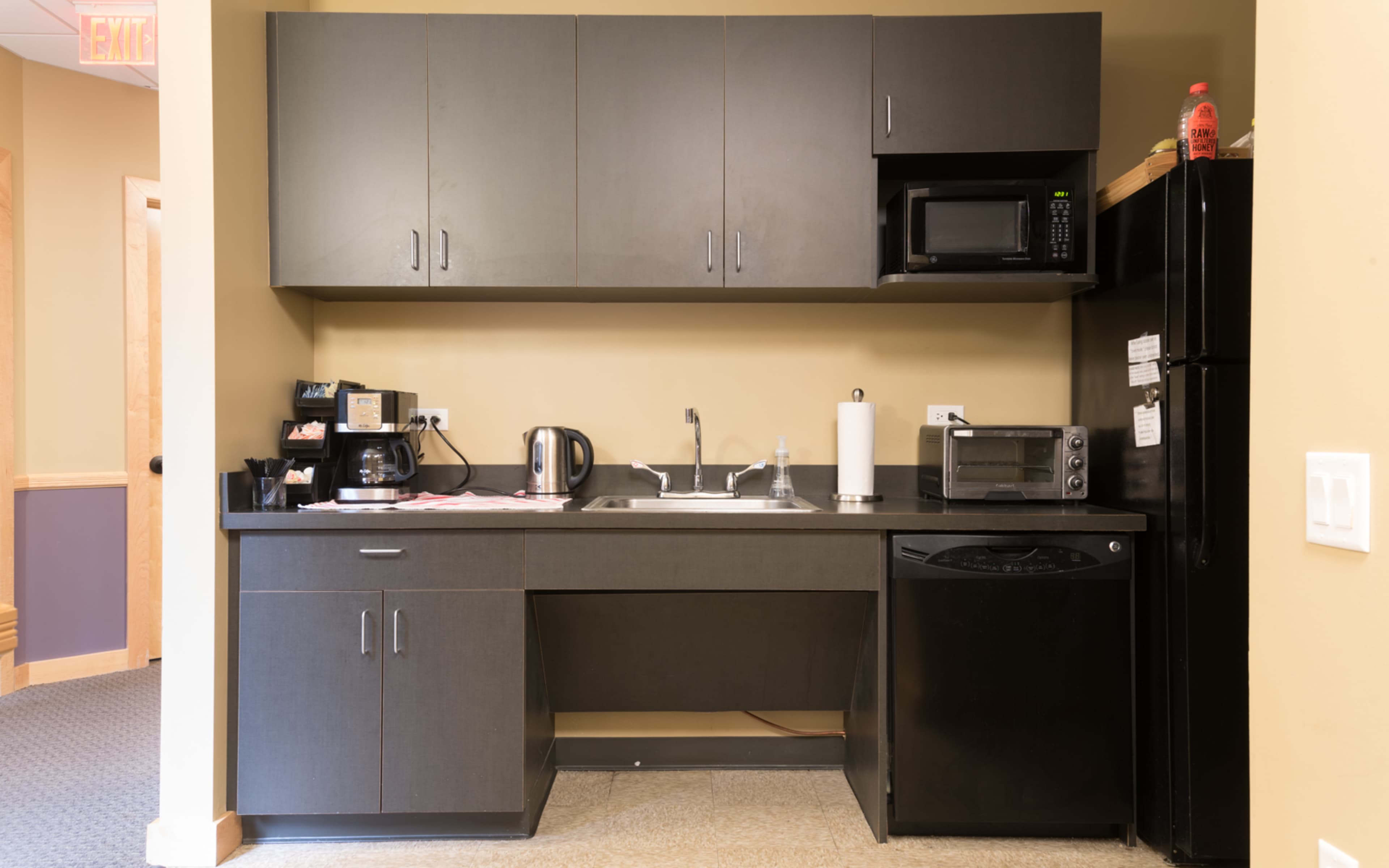 A small kitchen area featuring dark cabinetry, a sink, a coffee maker, a microwave, and a refrigerator.