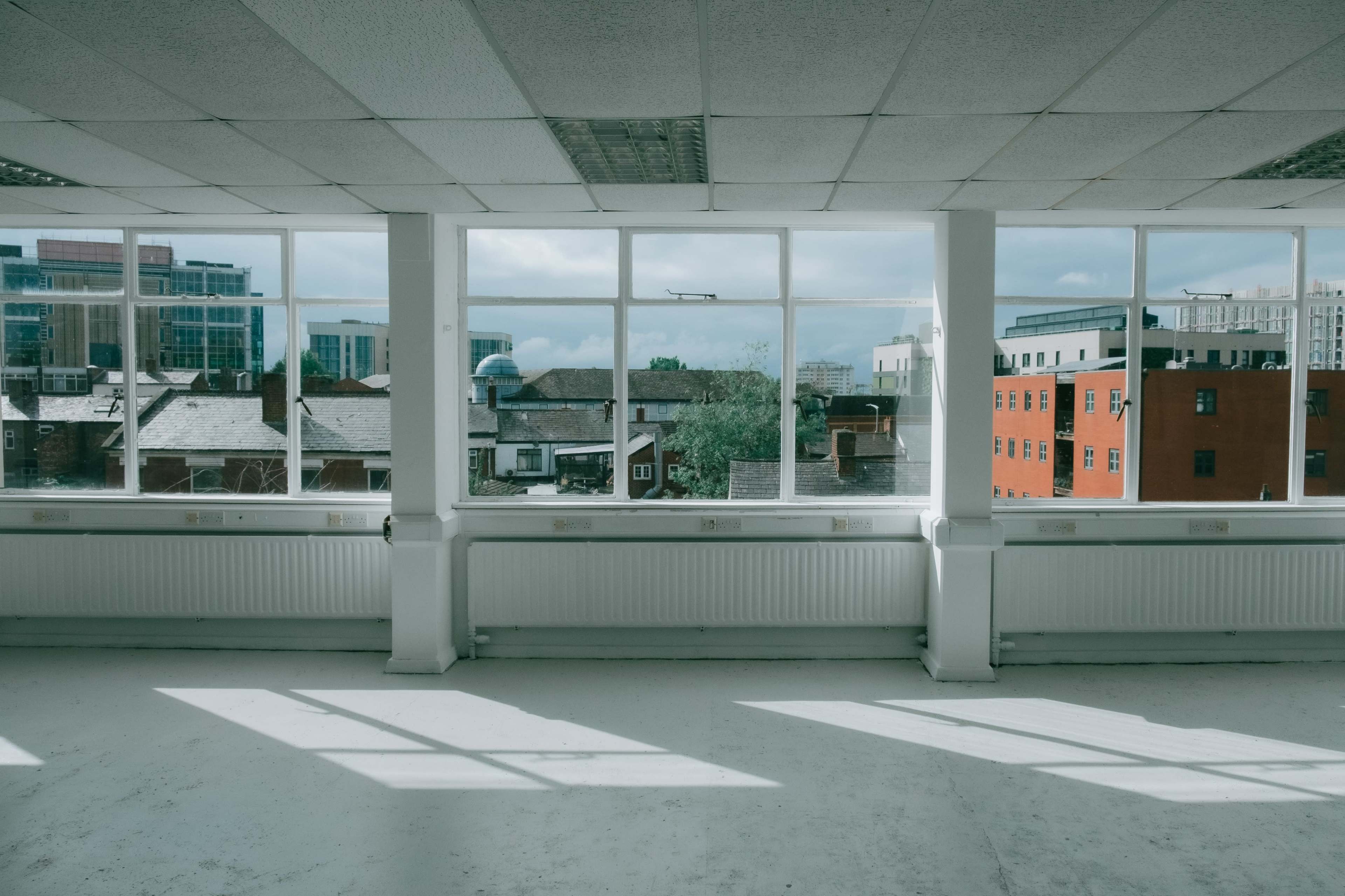 An empty office space with large windows overlooking a cityscape featuring buildings and rooftops.