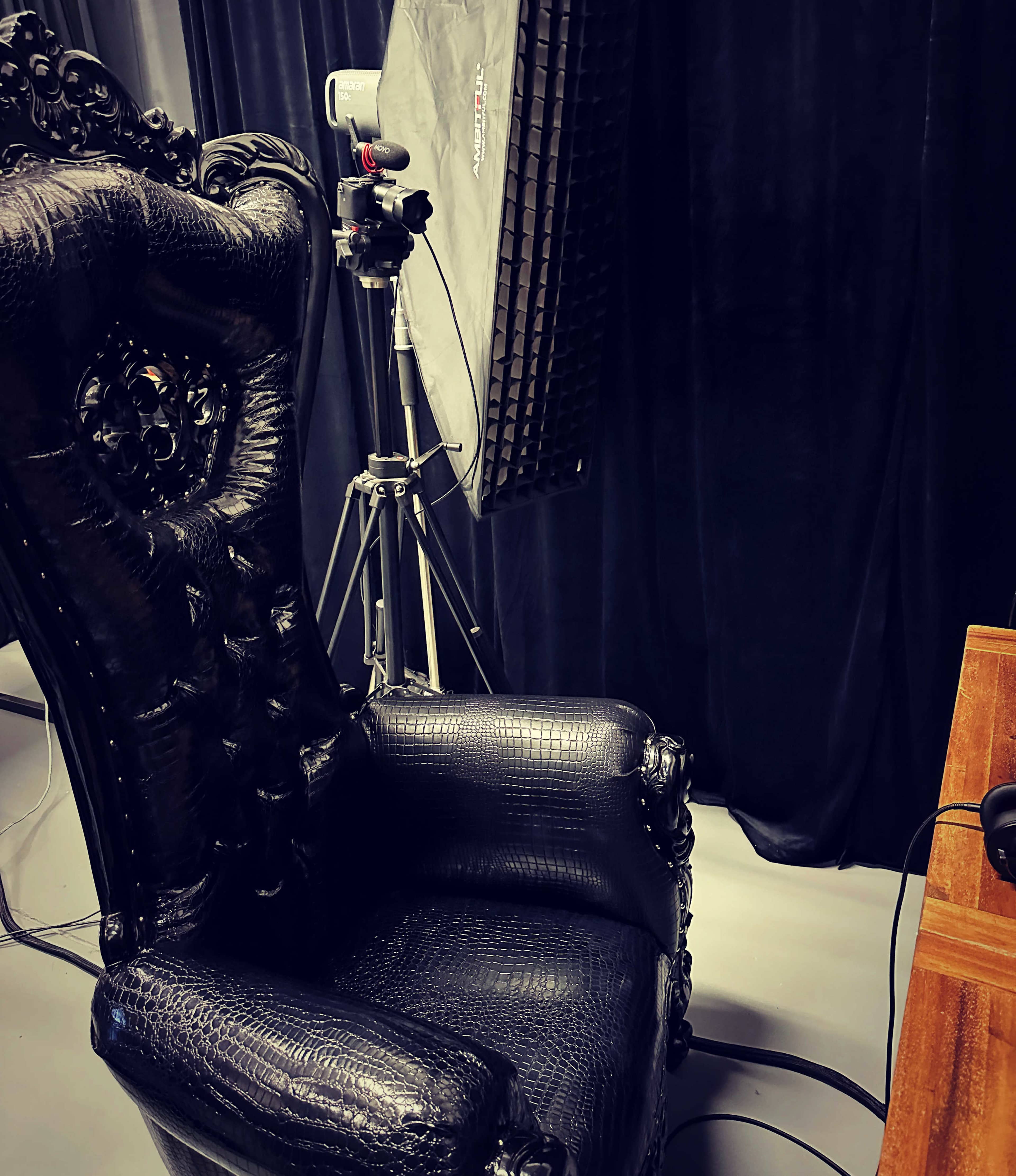 A decorative black chair beside a camera and a lighting setup against a dark backdrop.