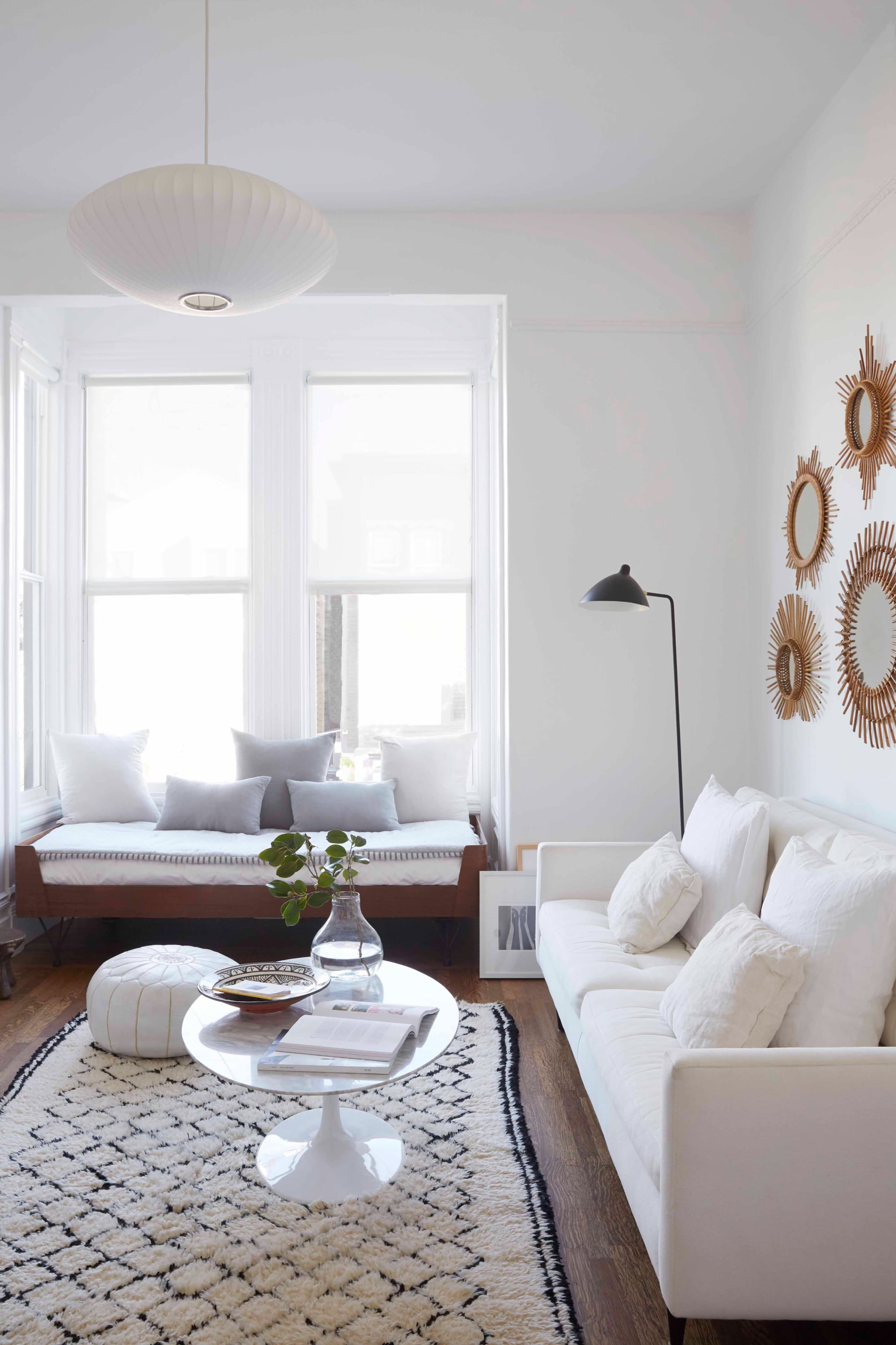 The image features a bright, minimalist living room with a white sofa, a round coffee table, and decorative mirrors on the wall.