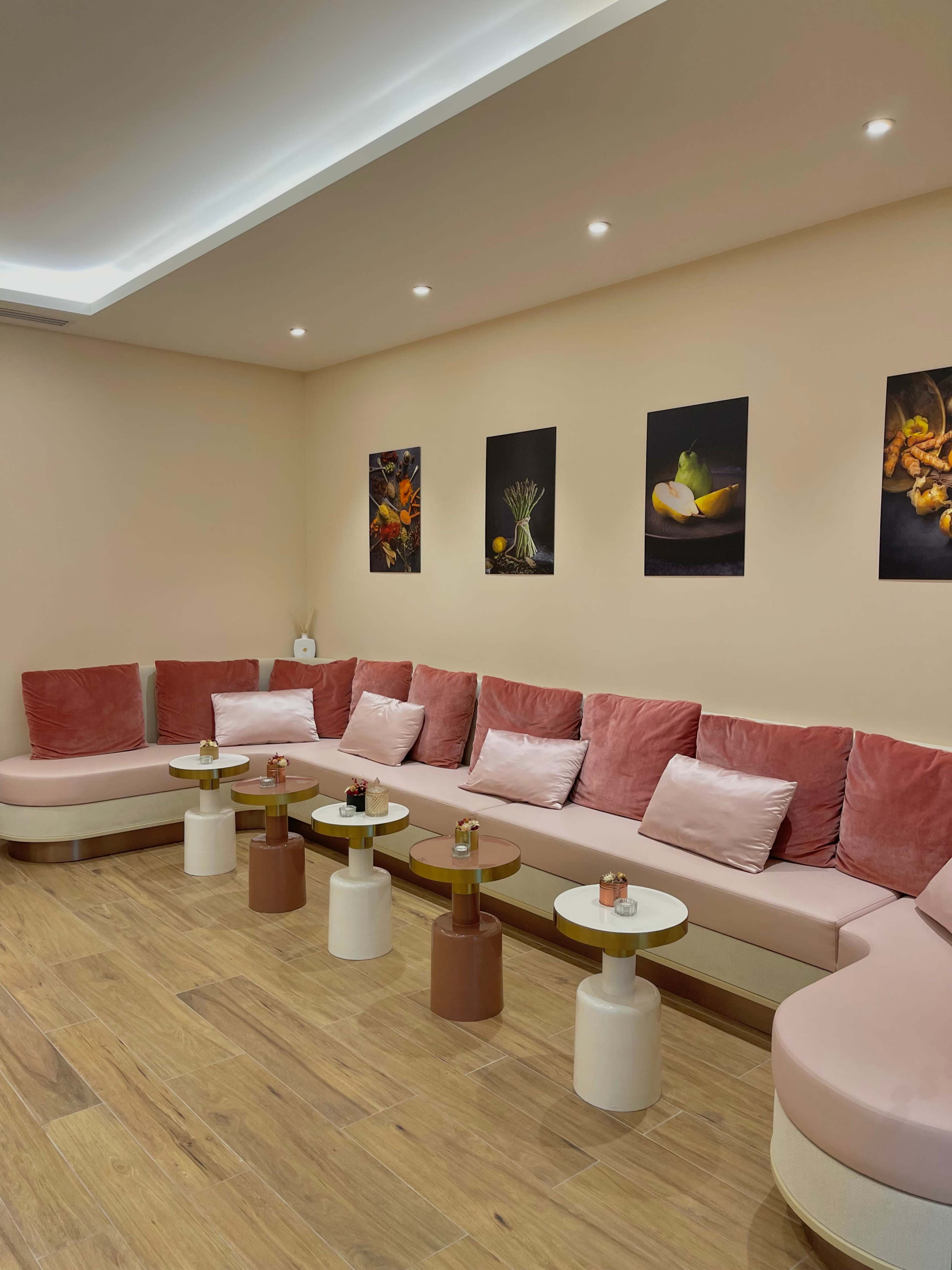 The scene features a modern lounge area with pink upholstered seating, small round tables, and framed food photography on the walls.