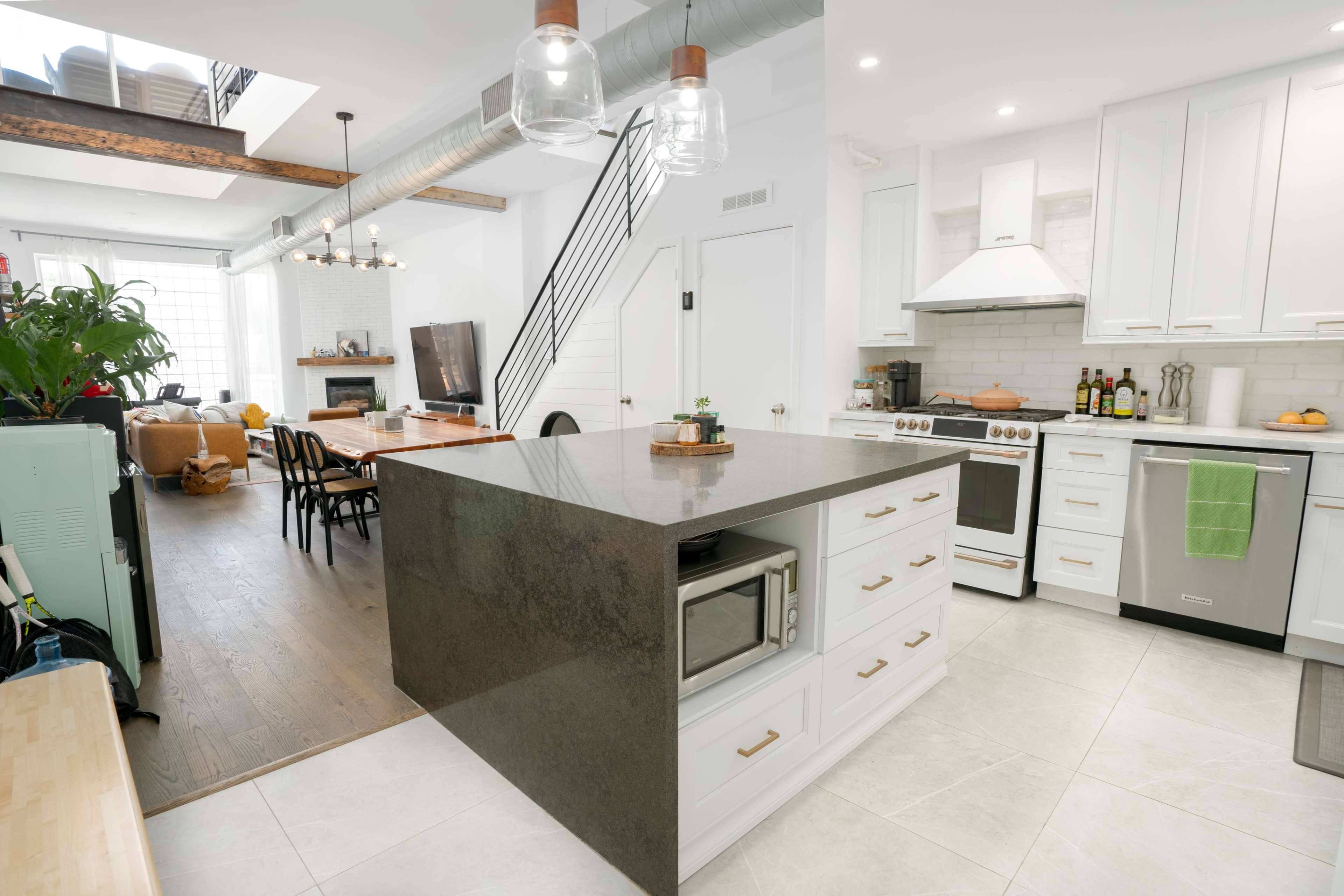 A modern kitchen with a large dark countertop island, white cabinets, and stainless steel appliances, connected to a cozy living area.
