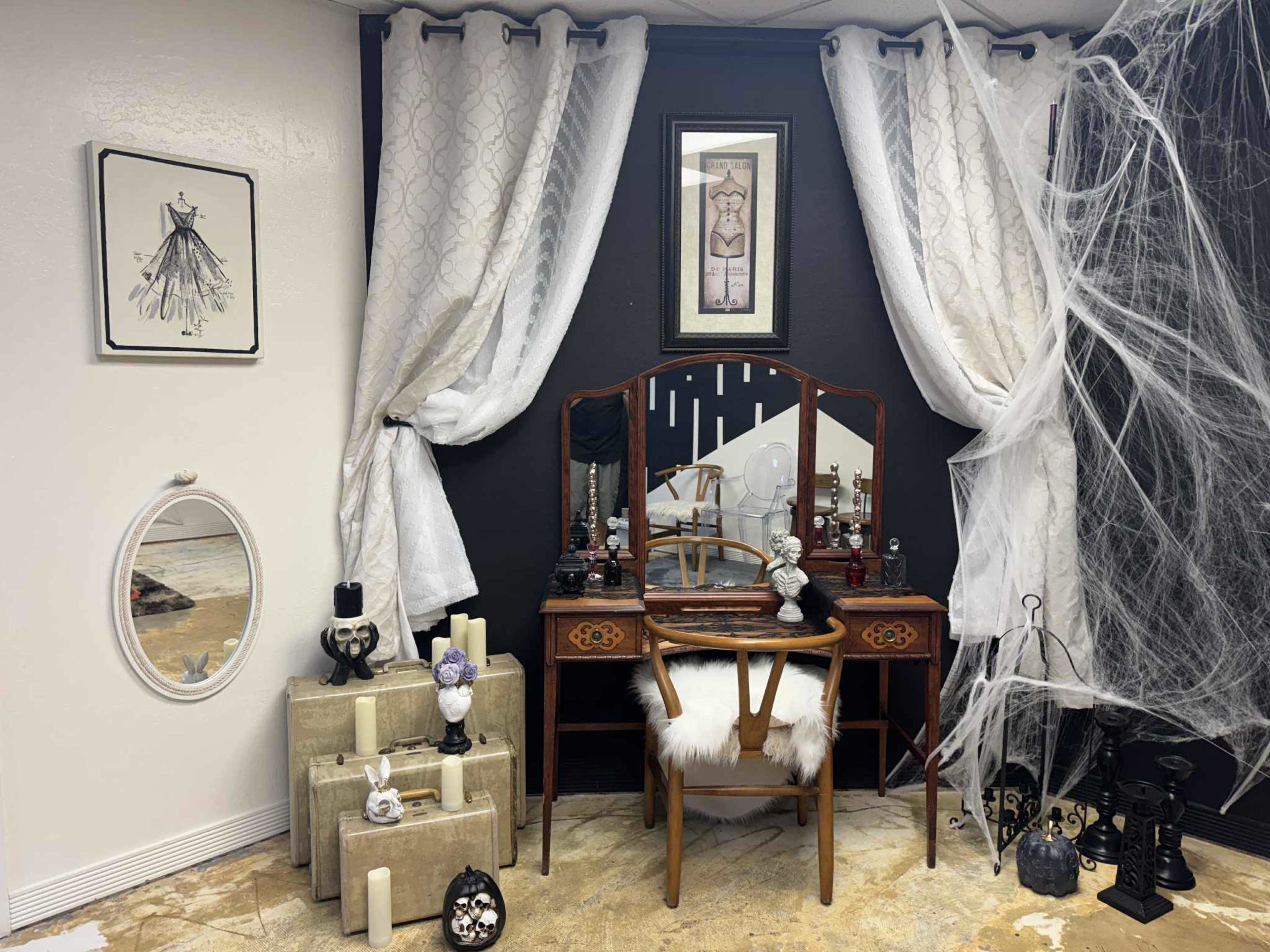 The image shows a vintage vanity table with a mirror, surrounded by decorative elements including candles and draped fabric, set in a dimly lit room.