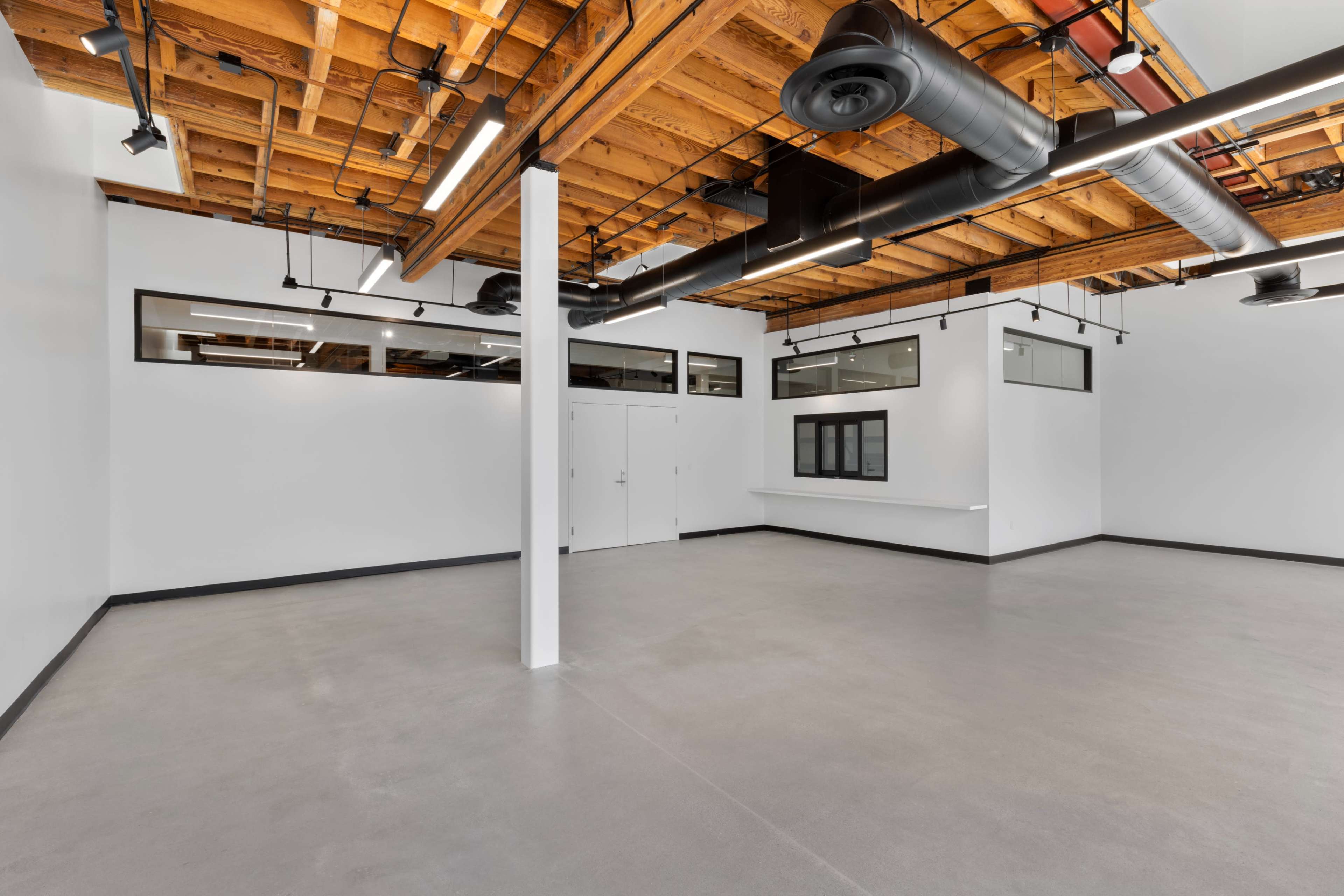 An empty room with a high wooden ceiling, grey concrete flooring, and large windows along the walls.