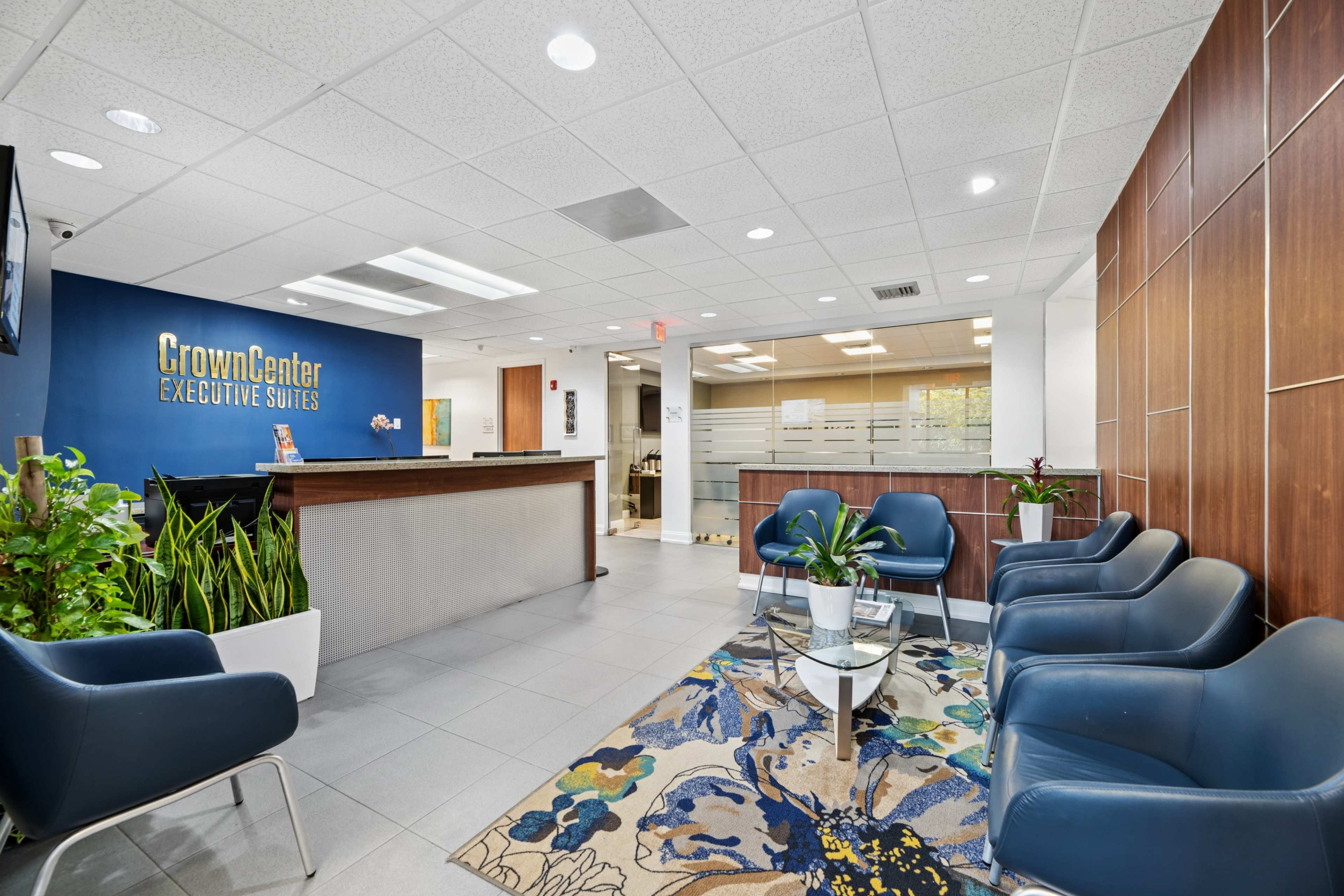The image features a modern reception area of an office space, with a front desk, seating chairs, and decorative plants.