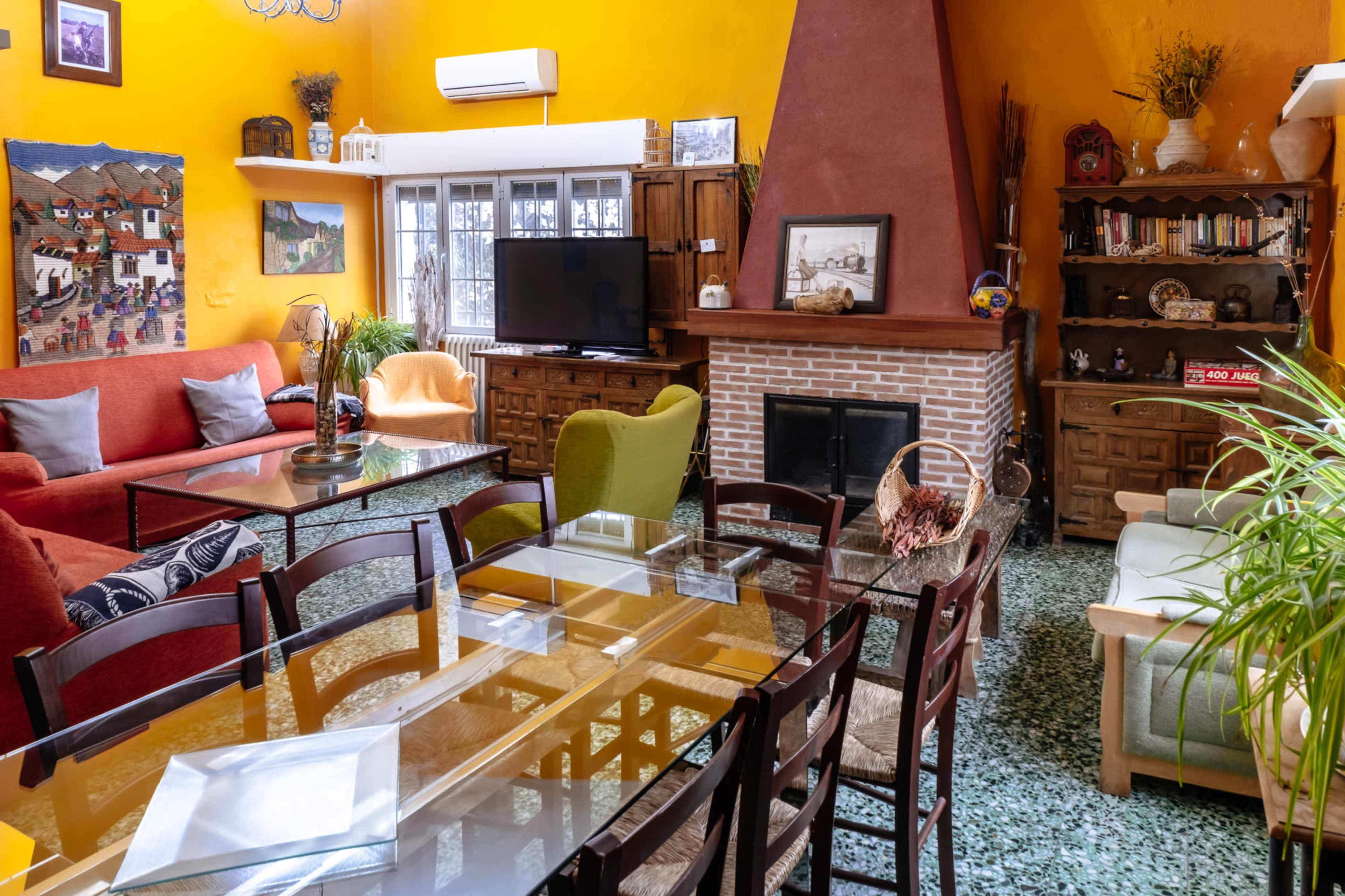 The scene depicts a cozy living space featuring a mix of colorful furniture, a fireplace, and a dining area with a glass table.