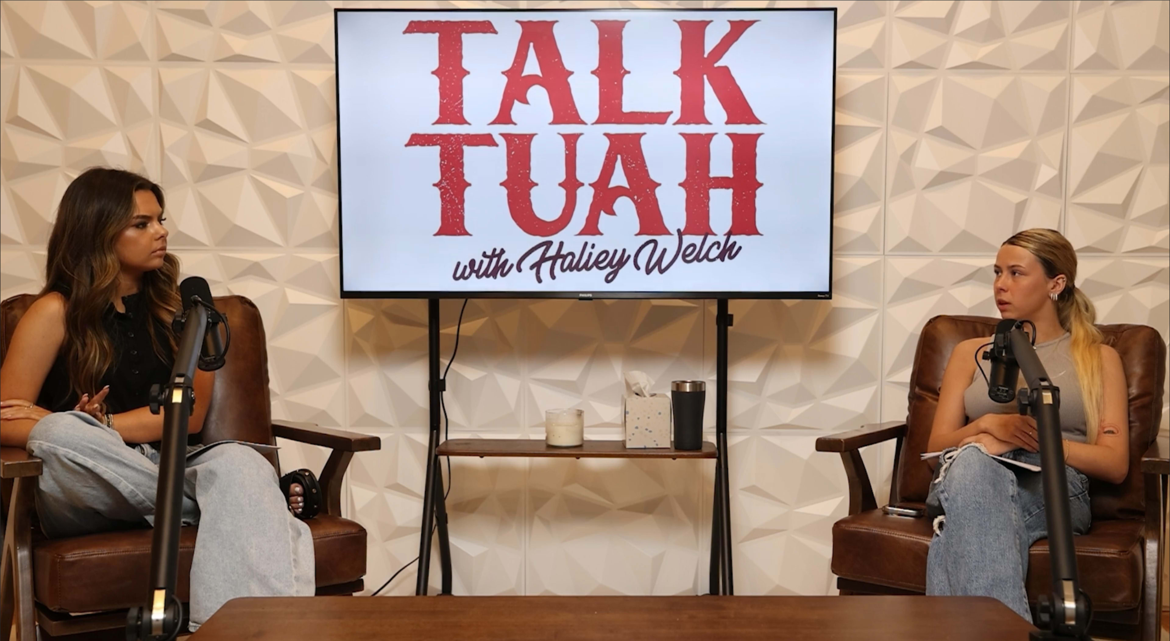 The image shows two women seated in armchairs in a studio setting, with a screen in the background displaying the title "TALK TUAH with Ashley Welch."
