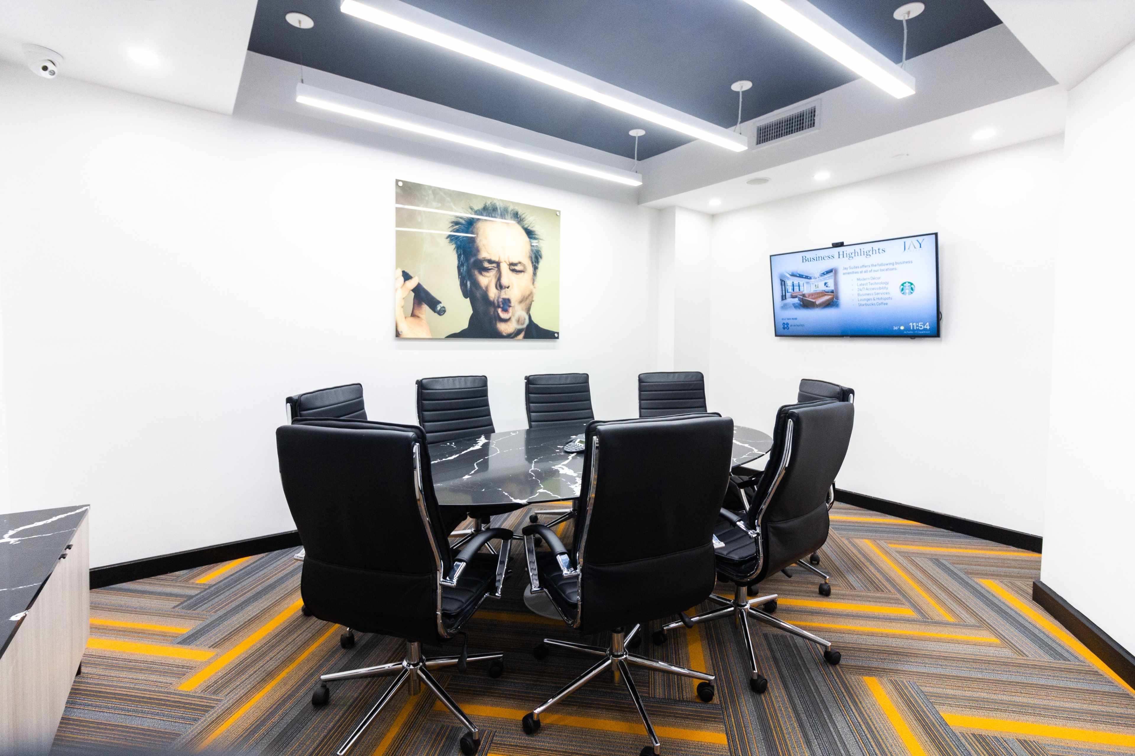 A modern conference room features a large black marble table surrounded by eight leather chairs, with an artwork and a screen displaying presentations on the walls.