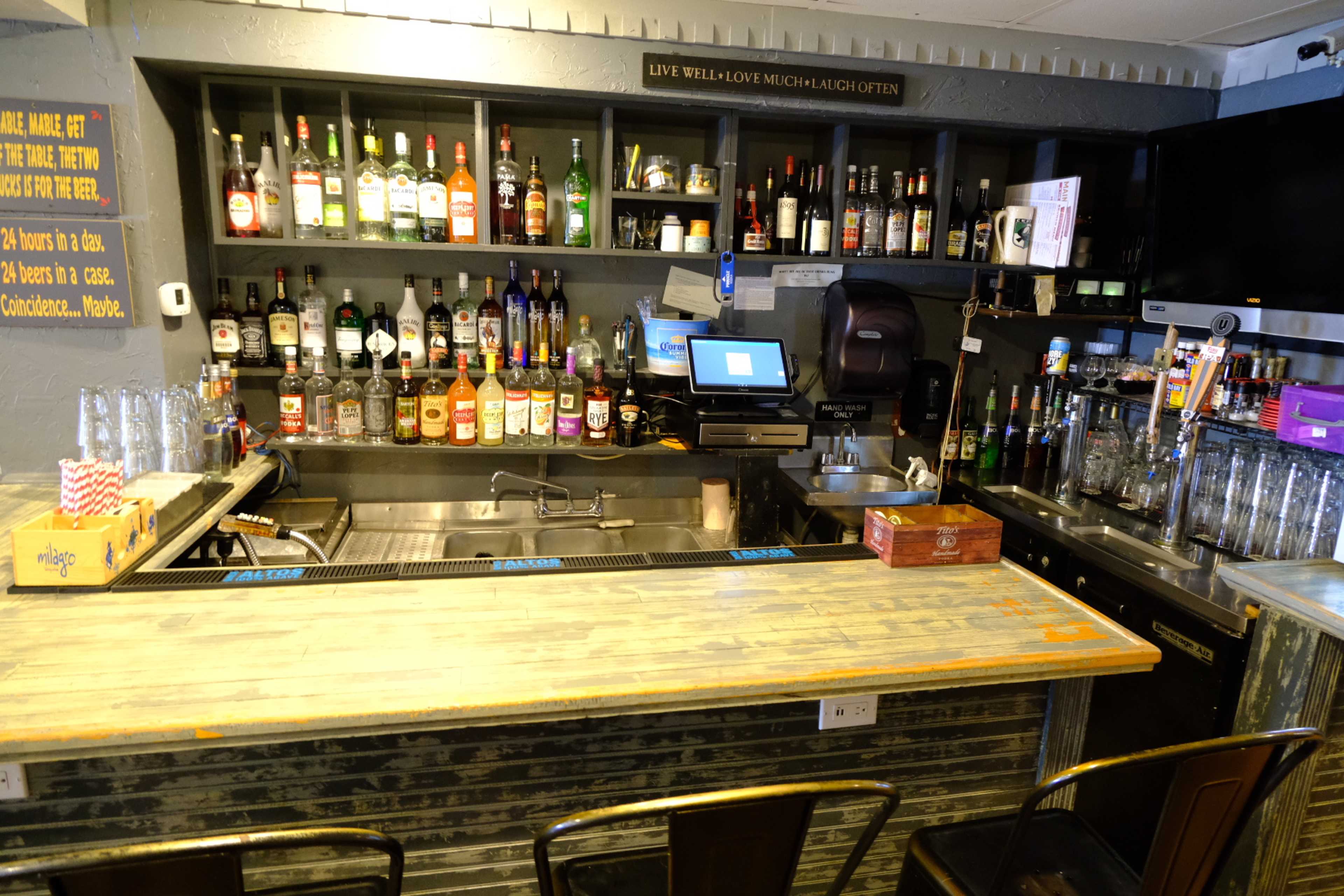 A well-organized bar with various bottles of liquor displayed on shelves behind the counter and a cash register on the bar surface.