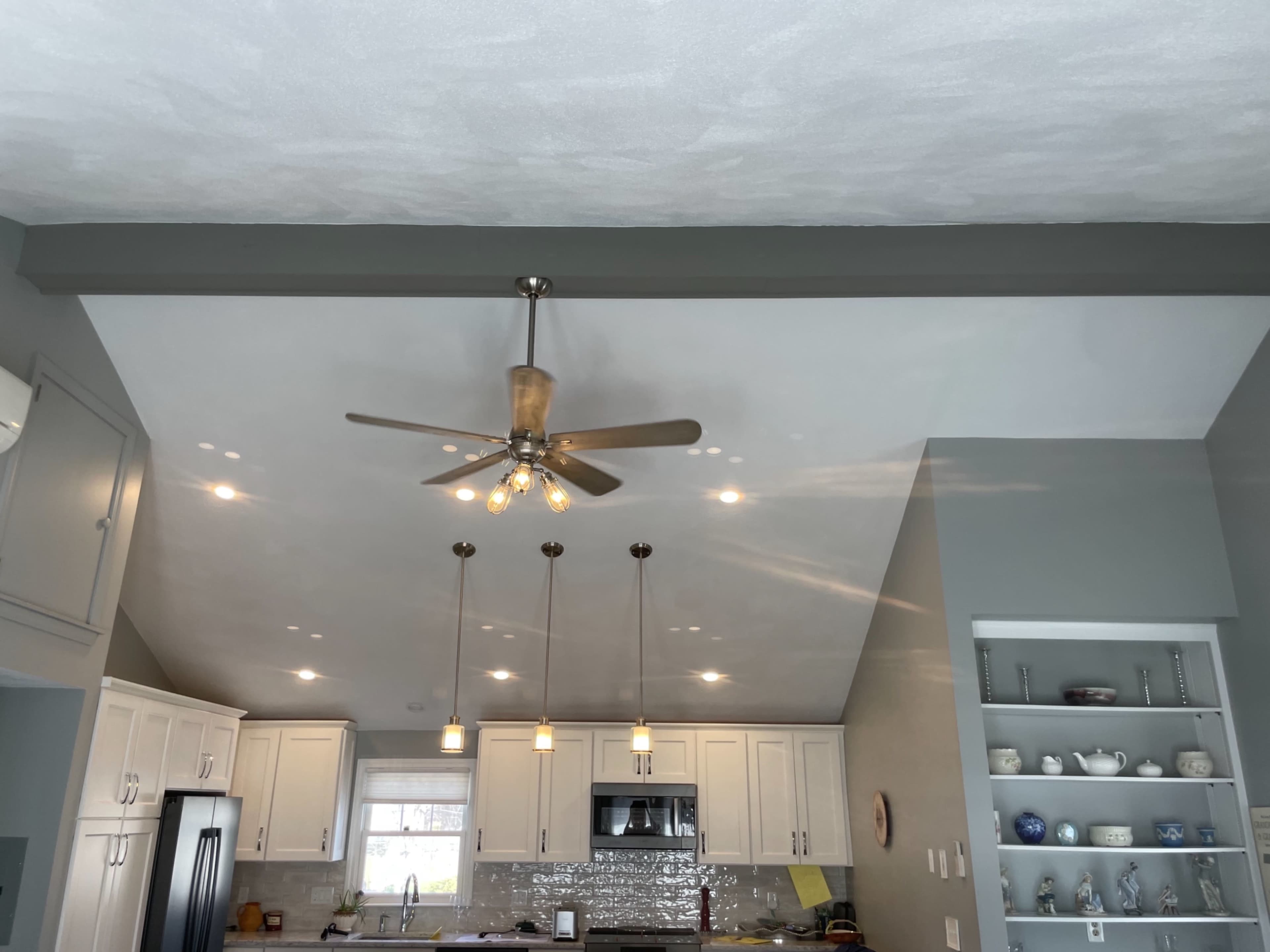 A kitchen with a sloped ceiling, featuring a ceiling fan, recessed lighting, and white cabinetry.